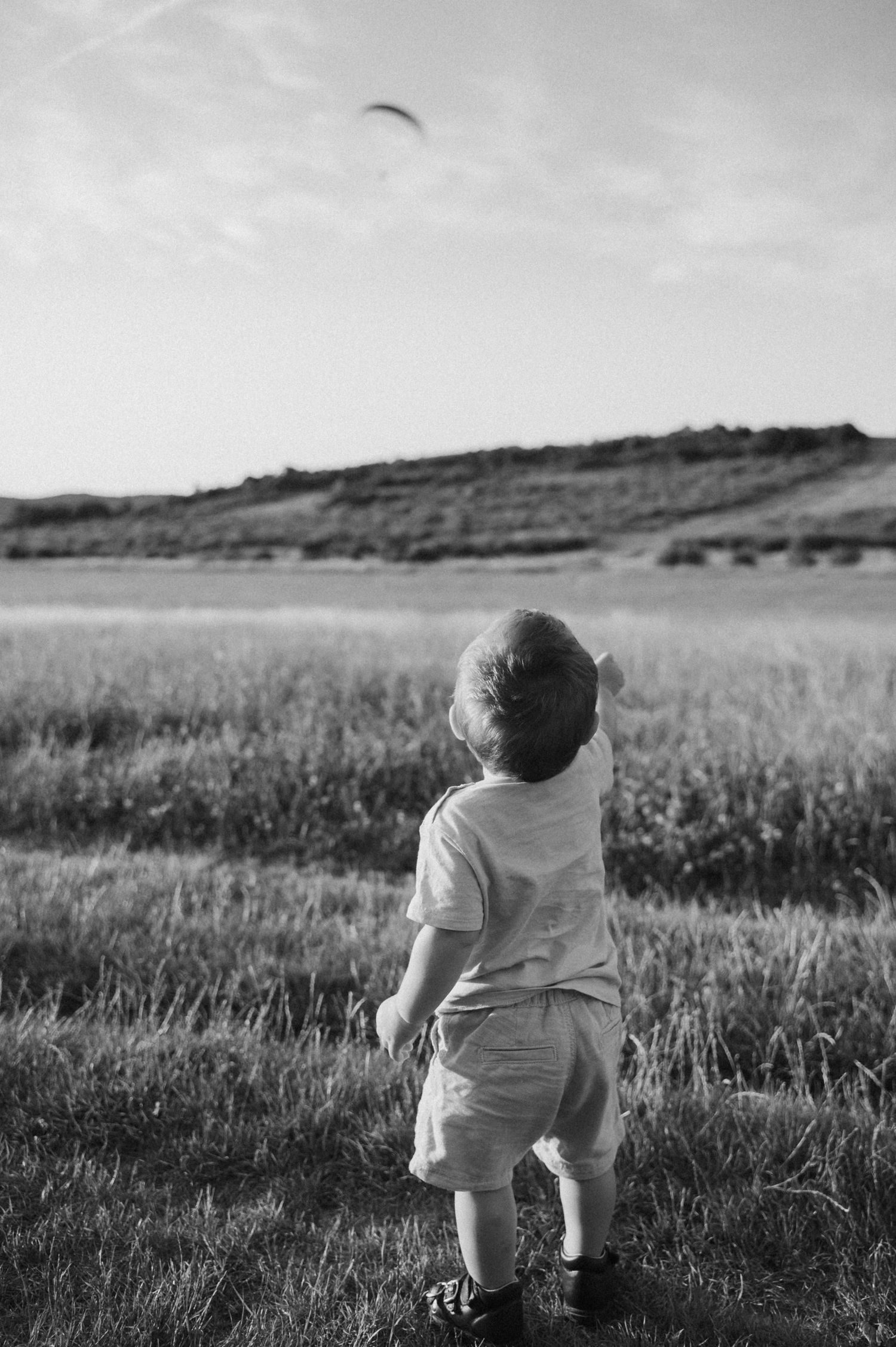 Black and white image of children sitting in a grassy meadow with rolling hills in the background.