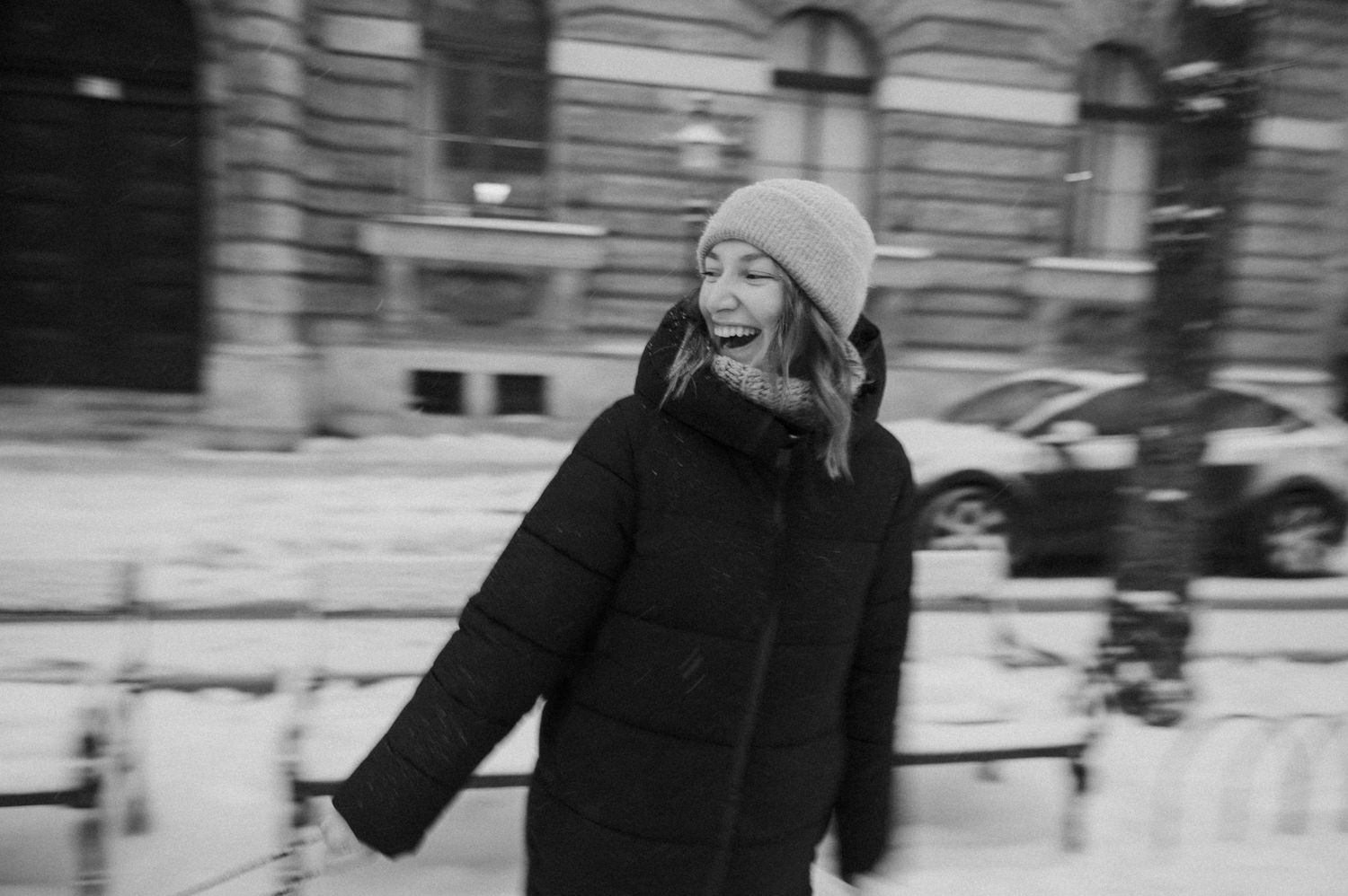 A person in winter clothing smiling while walking in the snow covered street.