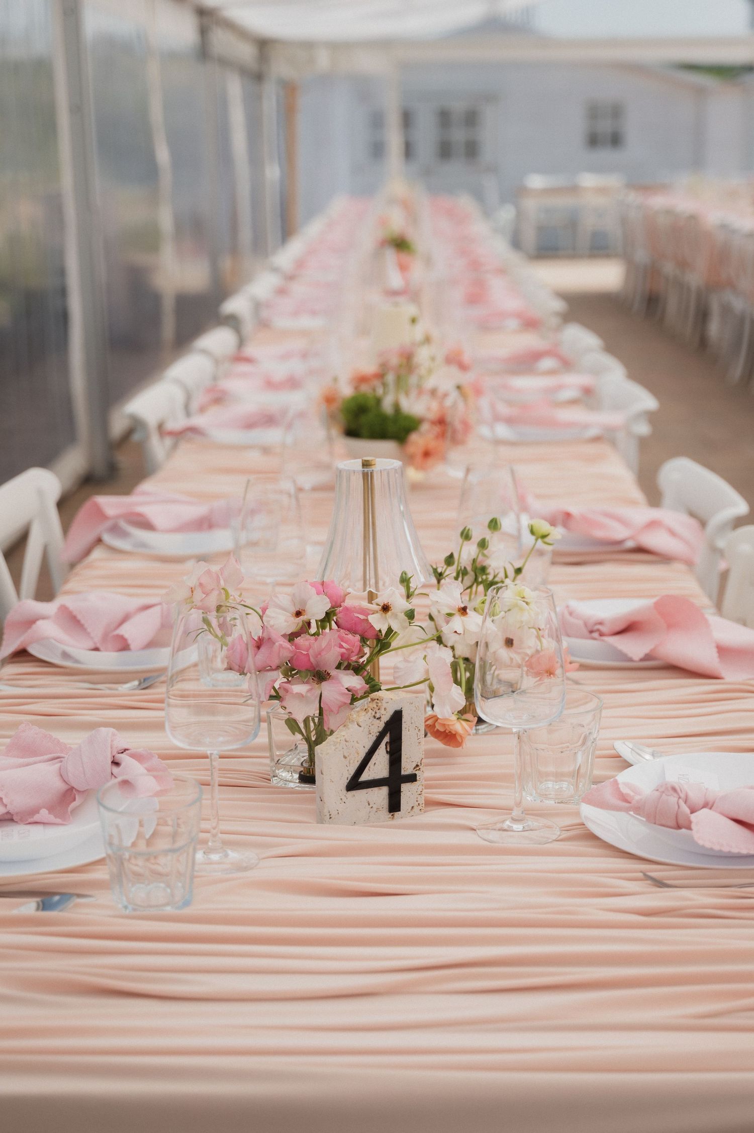Long wedding reception table with pink linens, floral centerpieces, and table number four marker.
