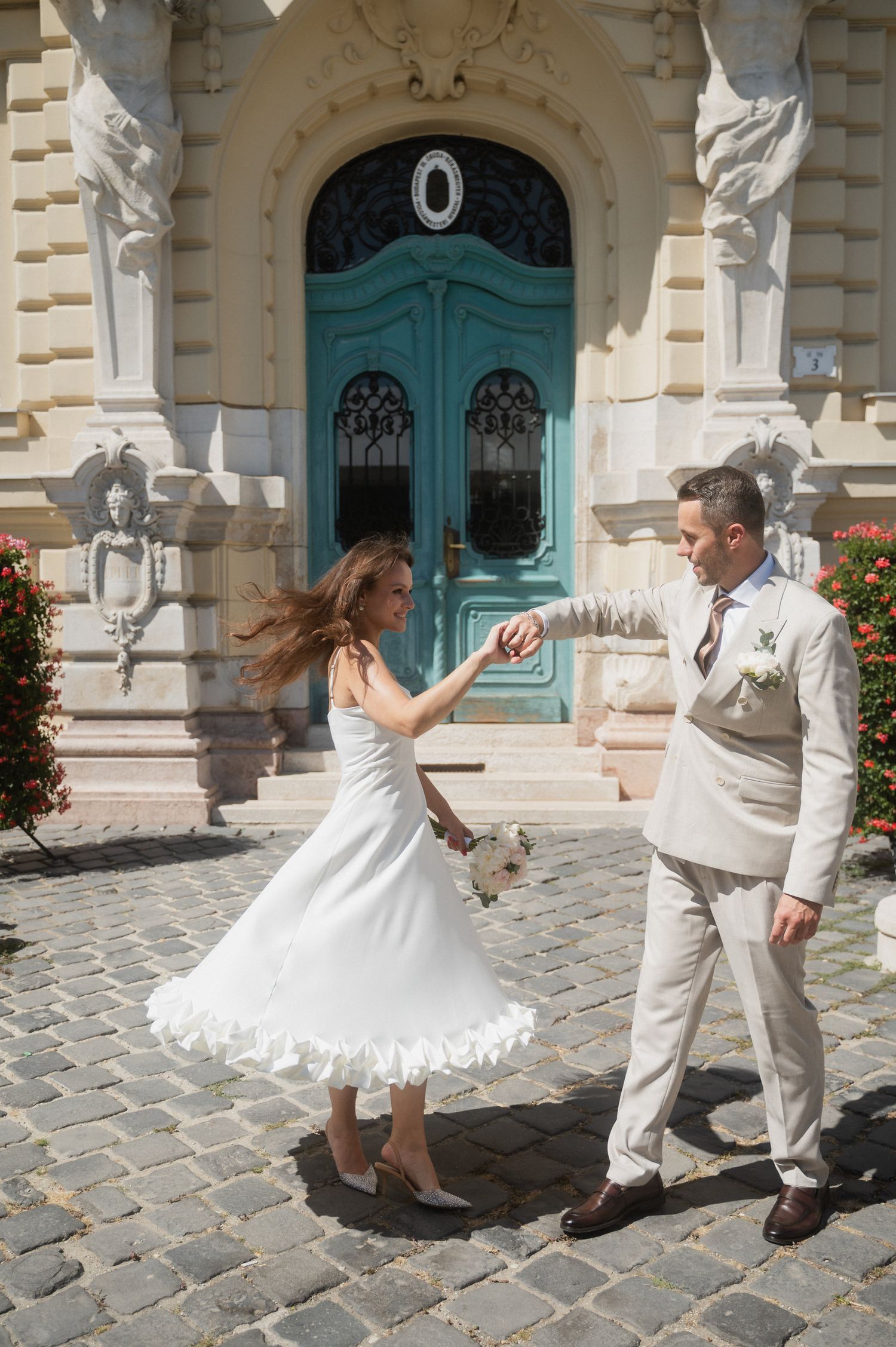 Wedding couple performs a fun dance sequence on cobblestone pavement outside a historic building.