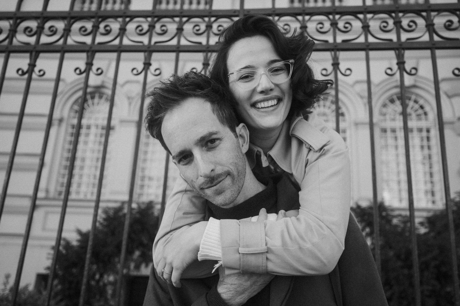 Three black and white photos show joyful moments between people embracing and smiling through ornate iron gates.