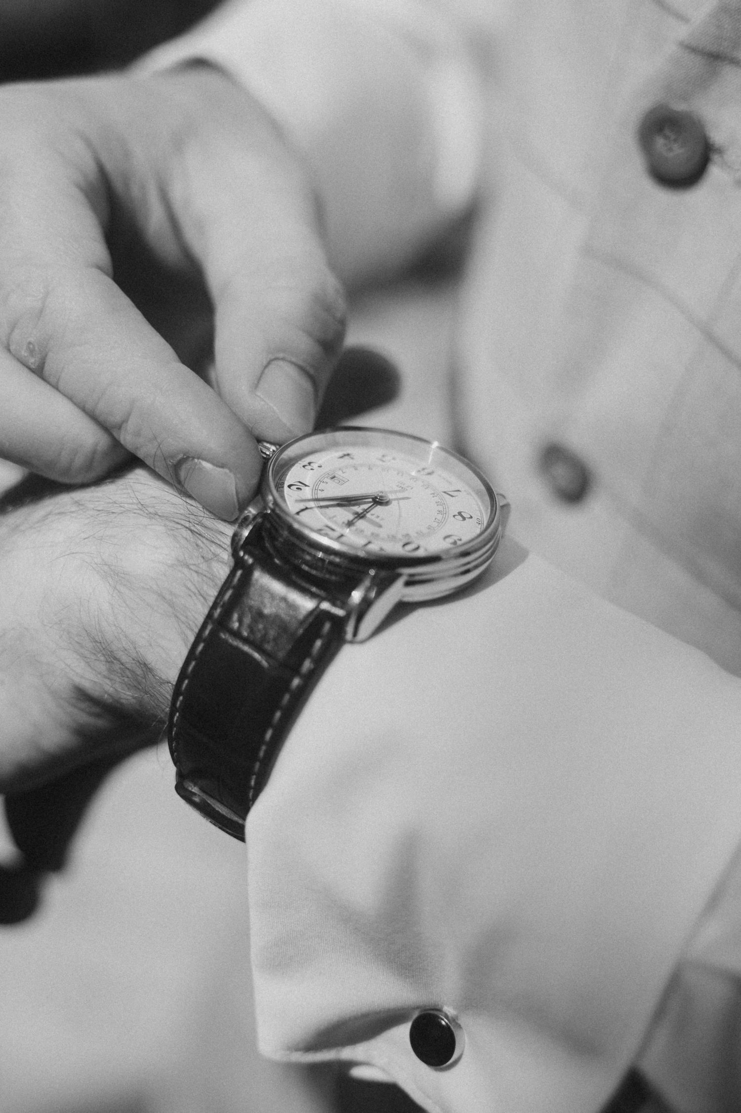 Close-up black and white photo showing hands examining and adjusting a leather strap wristwatch.