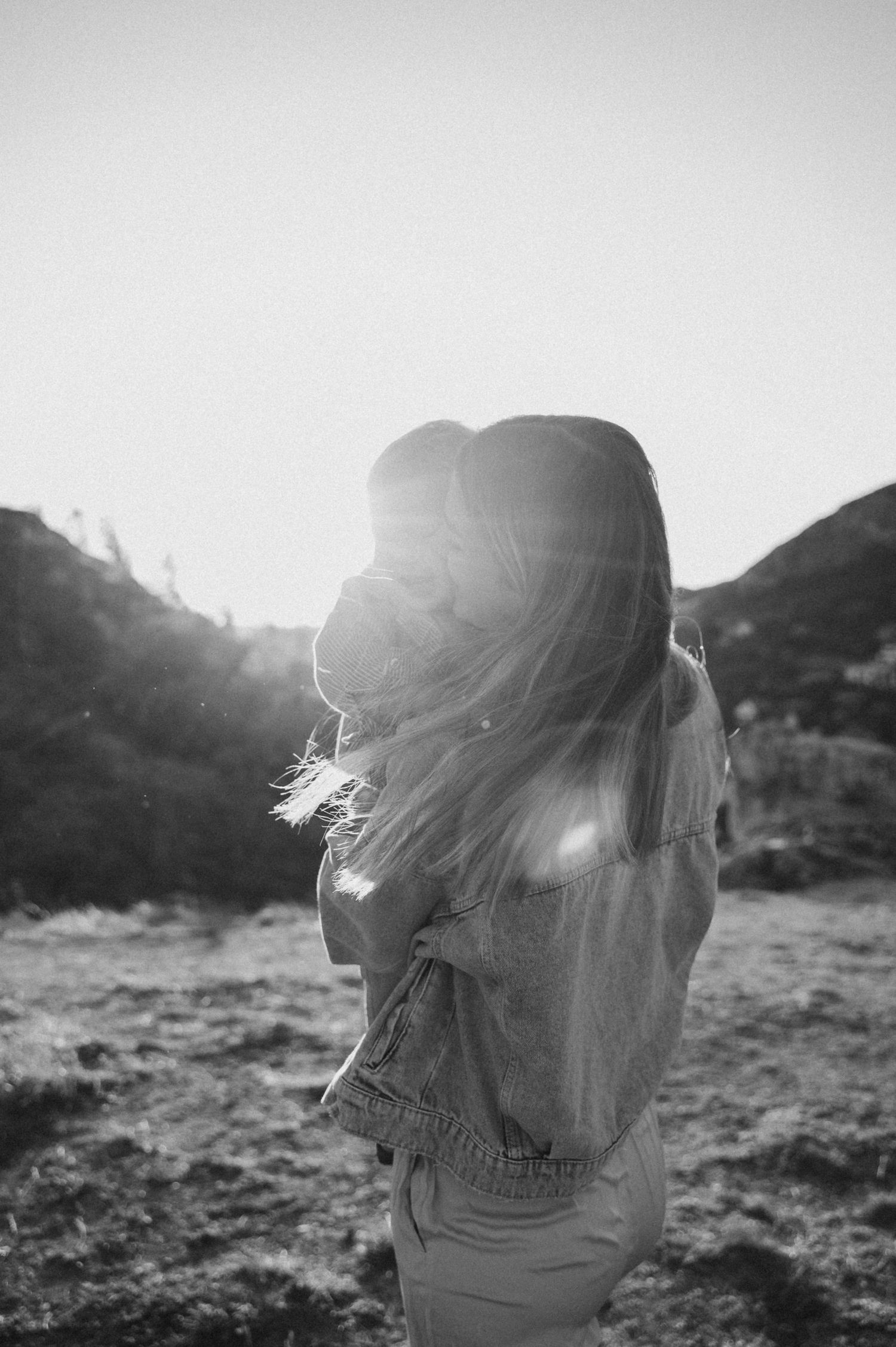 A silhouetted figure stands in a sunlit field with hair flowing in the wind at golden hour.