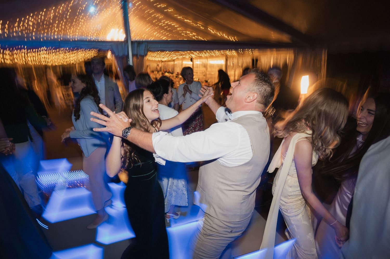 Guests dancing joyfully on a lit dance floor under string lights at a lively wedding reception.