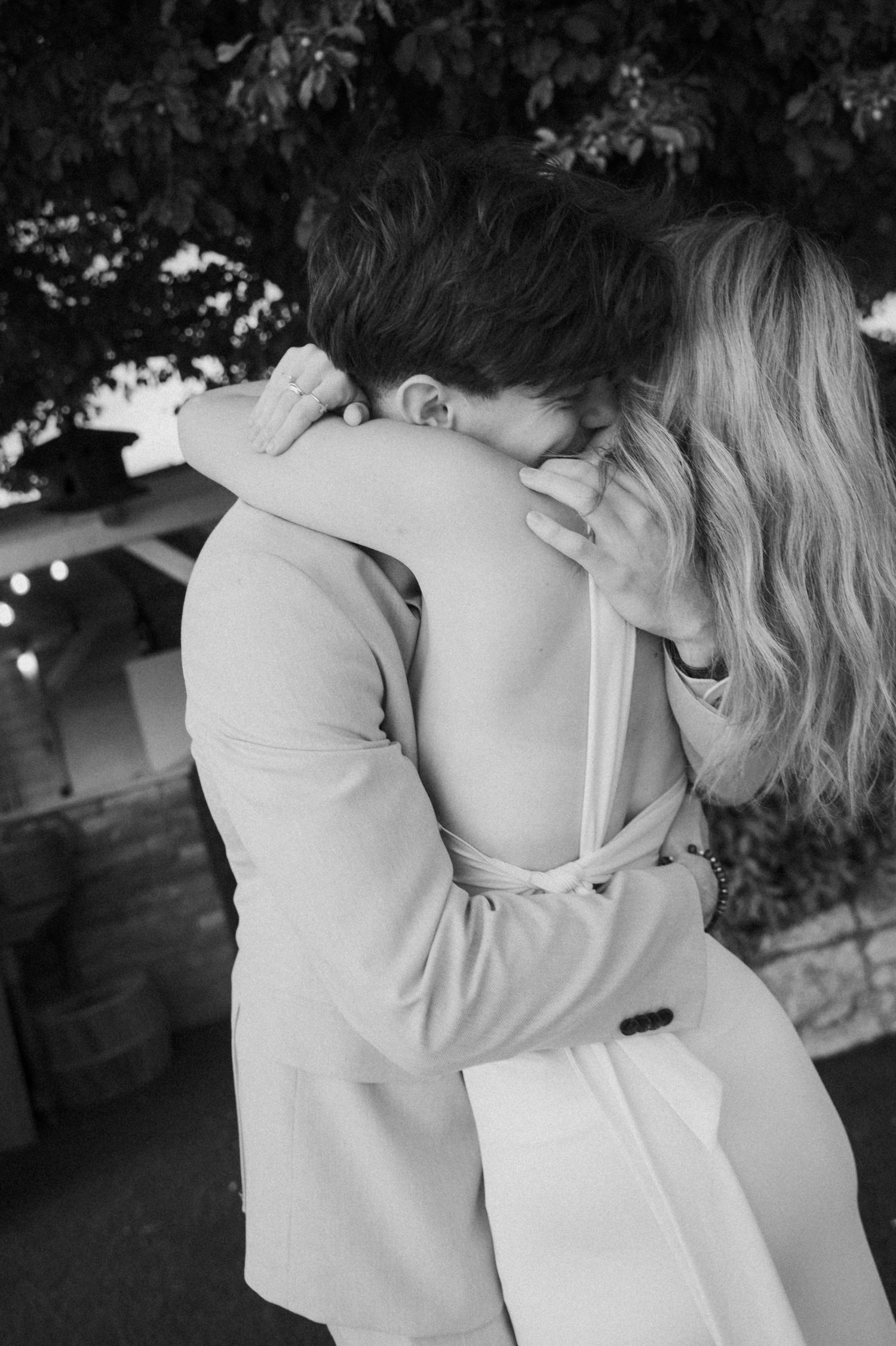 Black and white photo of a couple embracing and kissing at an outdoor wedding venue.