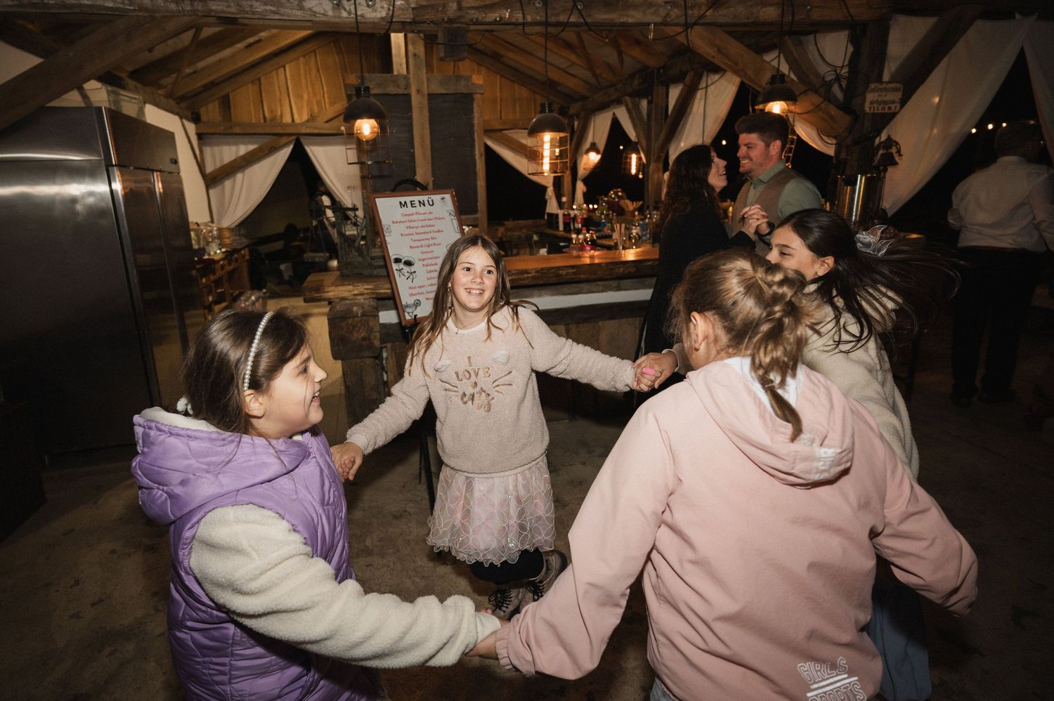 People holding hands in a circle dancing together in a rustic indoor setting with warm lighting.