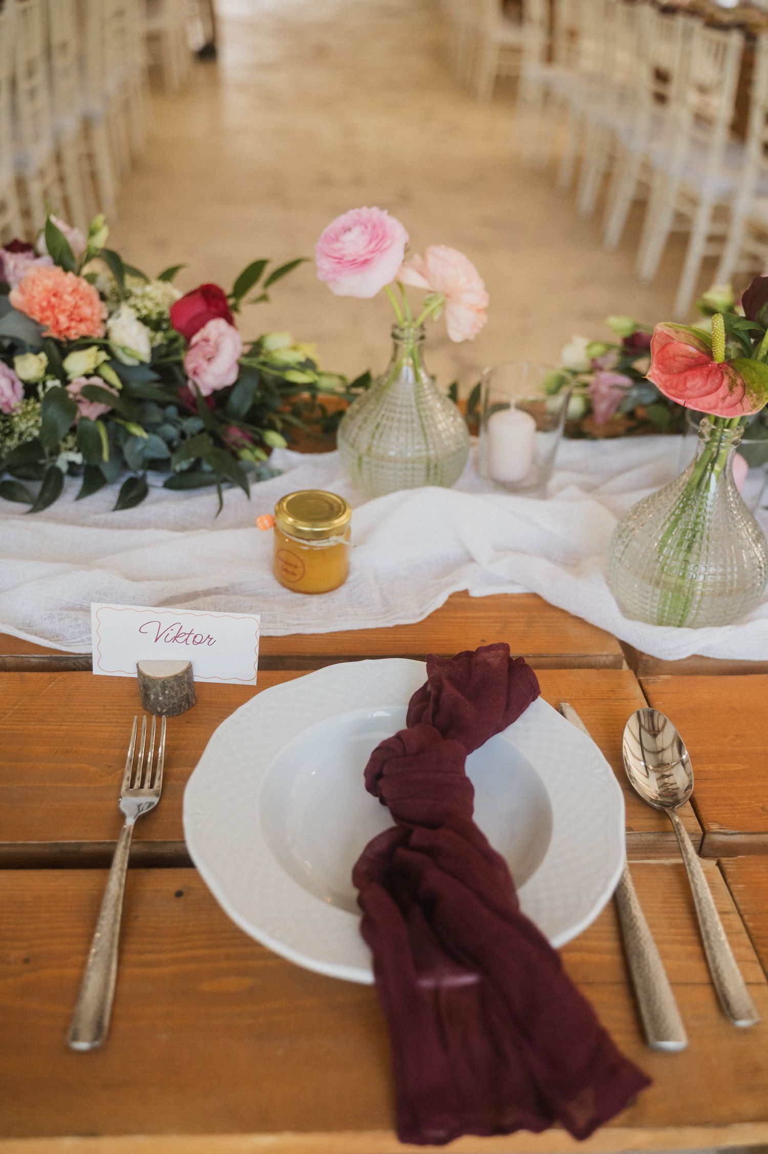 Elegant table setting with burgundy napkins, white plates, and delicate floral centerpieces on wooden tables.