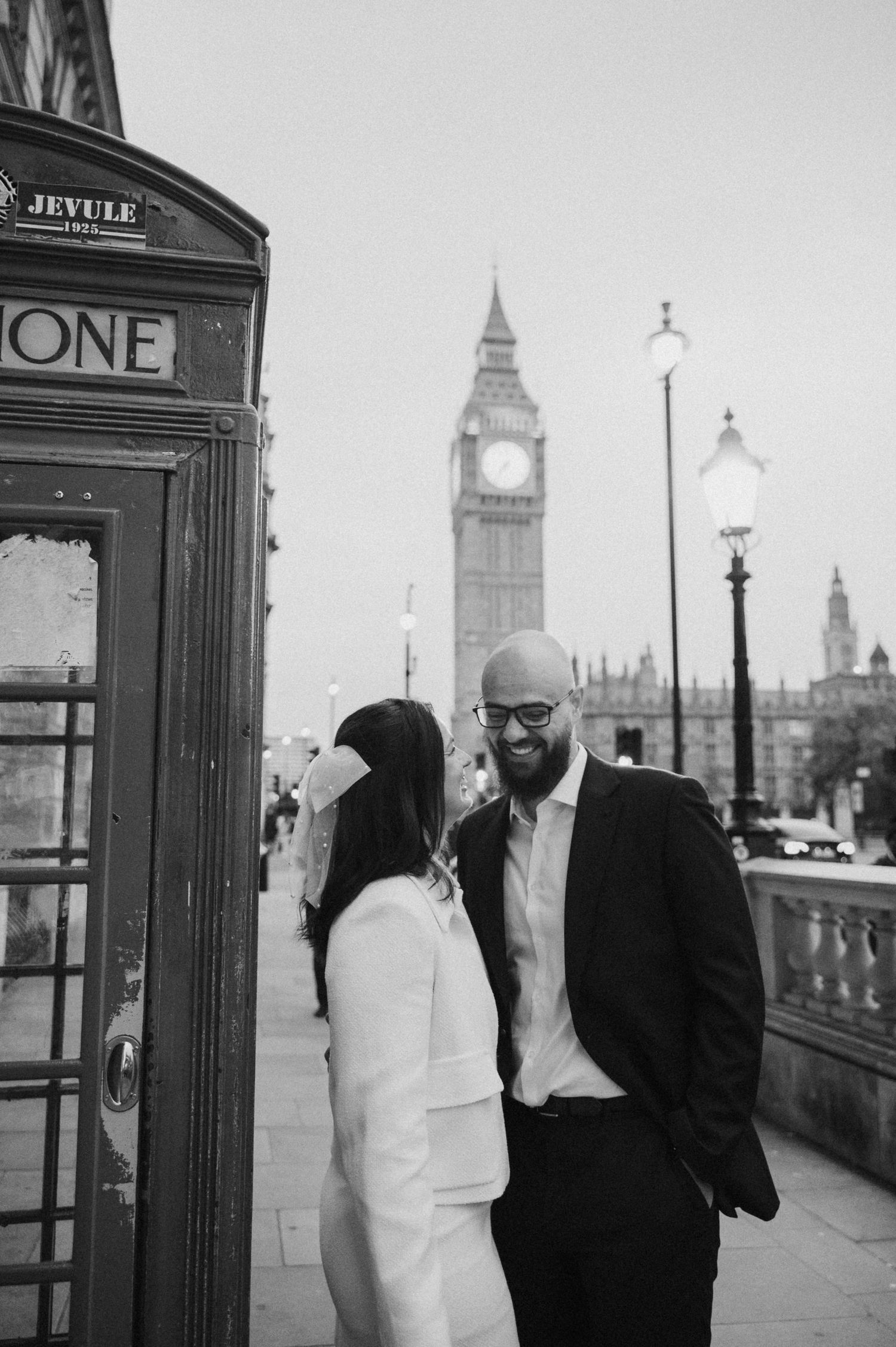 A black and white portrait of a couple by a London phone booth with Big Ben visible.