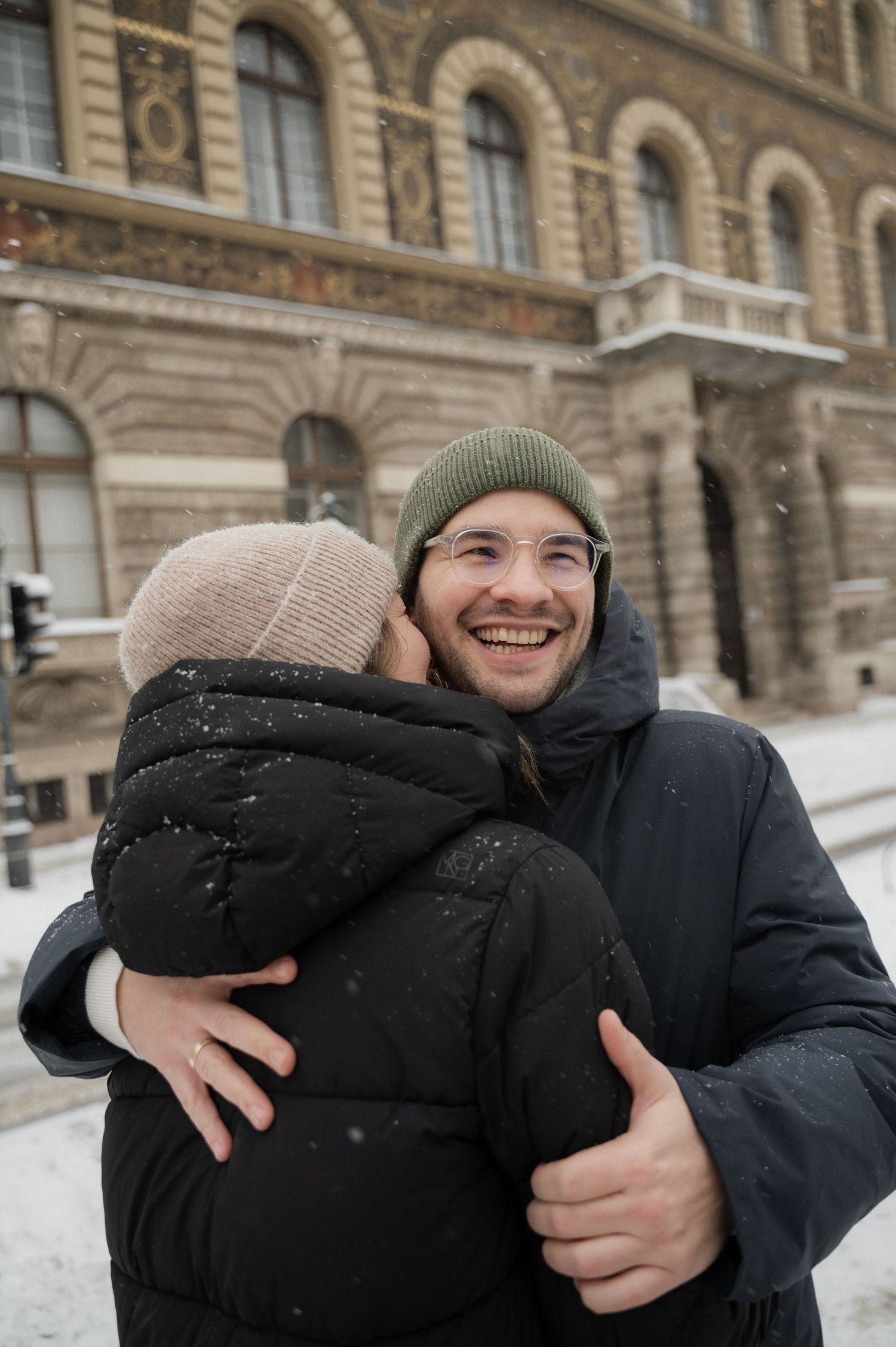 People in winter clothing sharing a joyful moment against historic architecture.