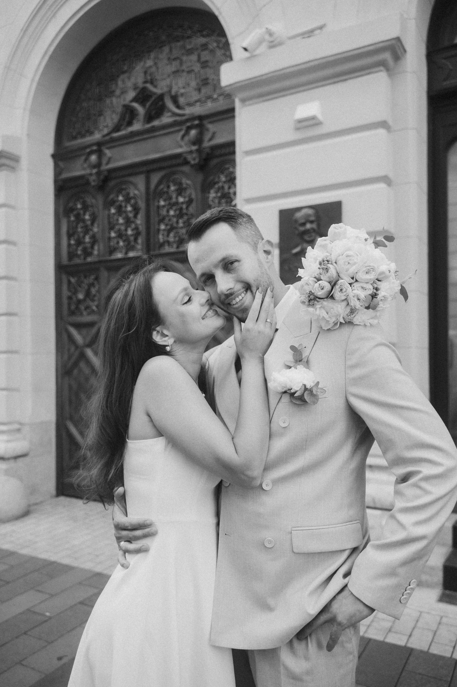 Tender moment between newlyweds against classical architectural backdrop.