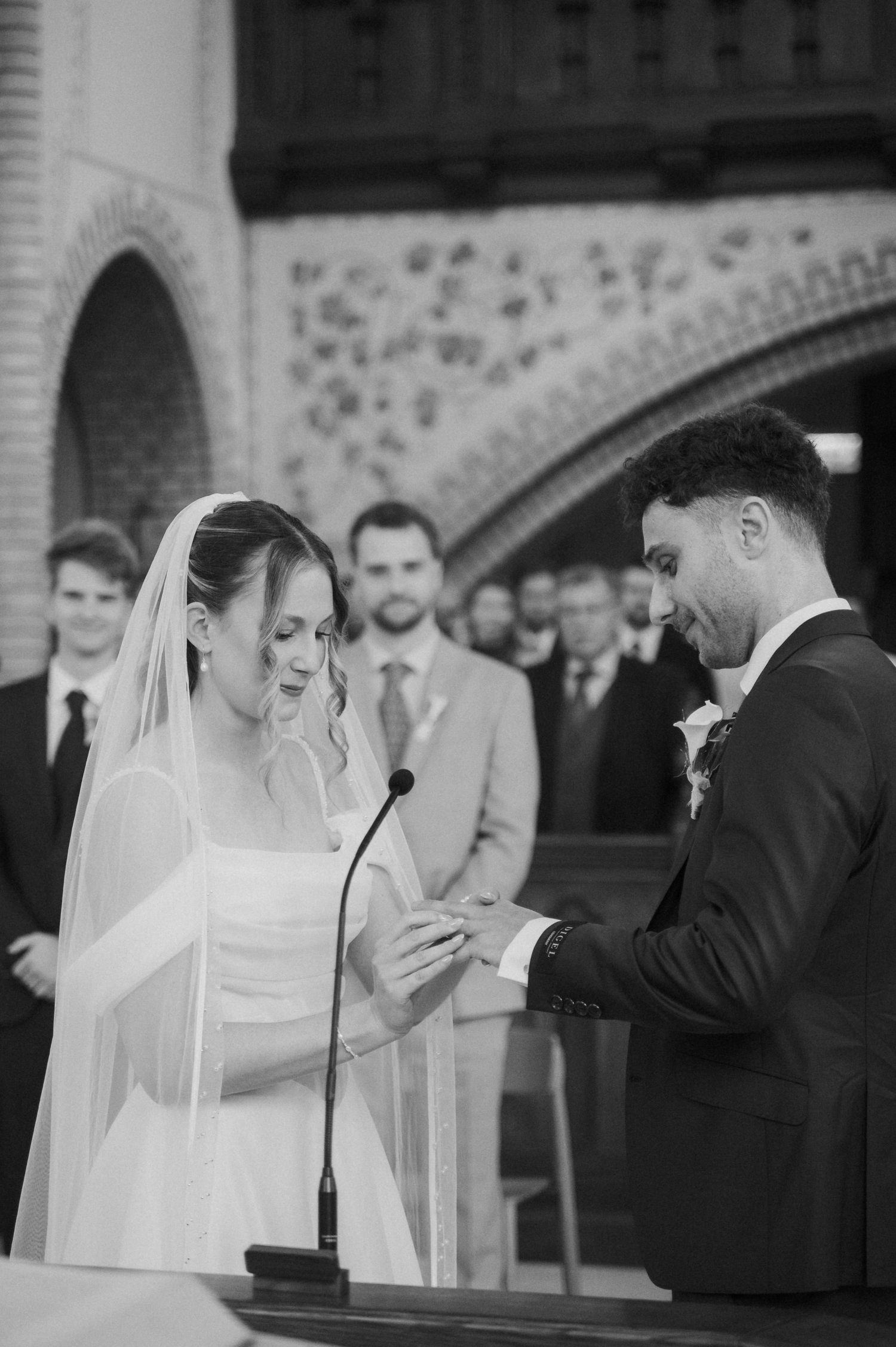 Bride and groom exchanging rings at altar during wedding ceremony in black and white photo.