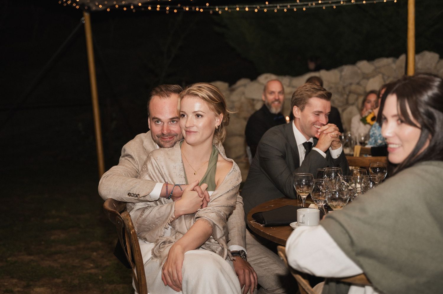 Wedding reception guests gather under string lights for an evening celebration.