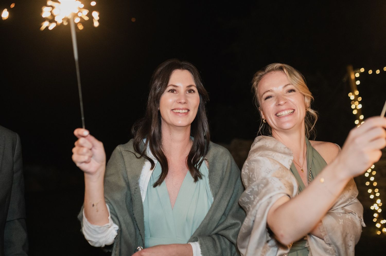 Wedding guests celebrating with sparklers at night under twinkling lights.