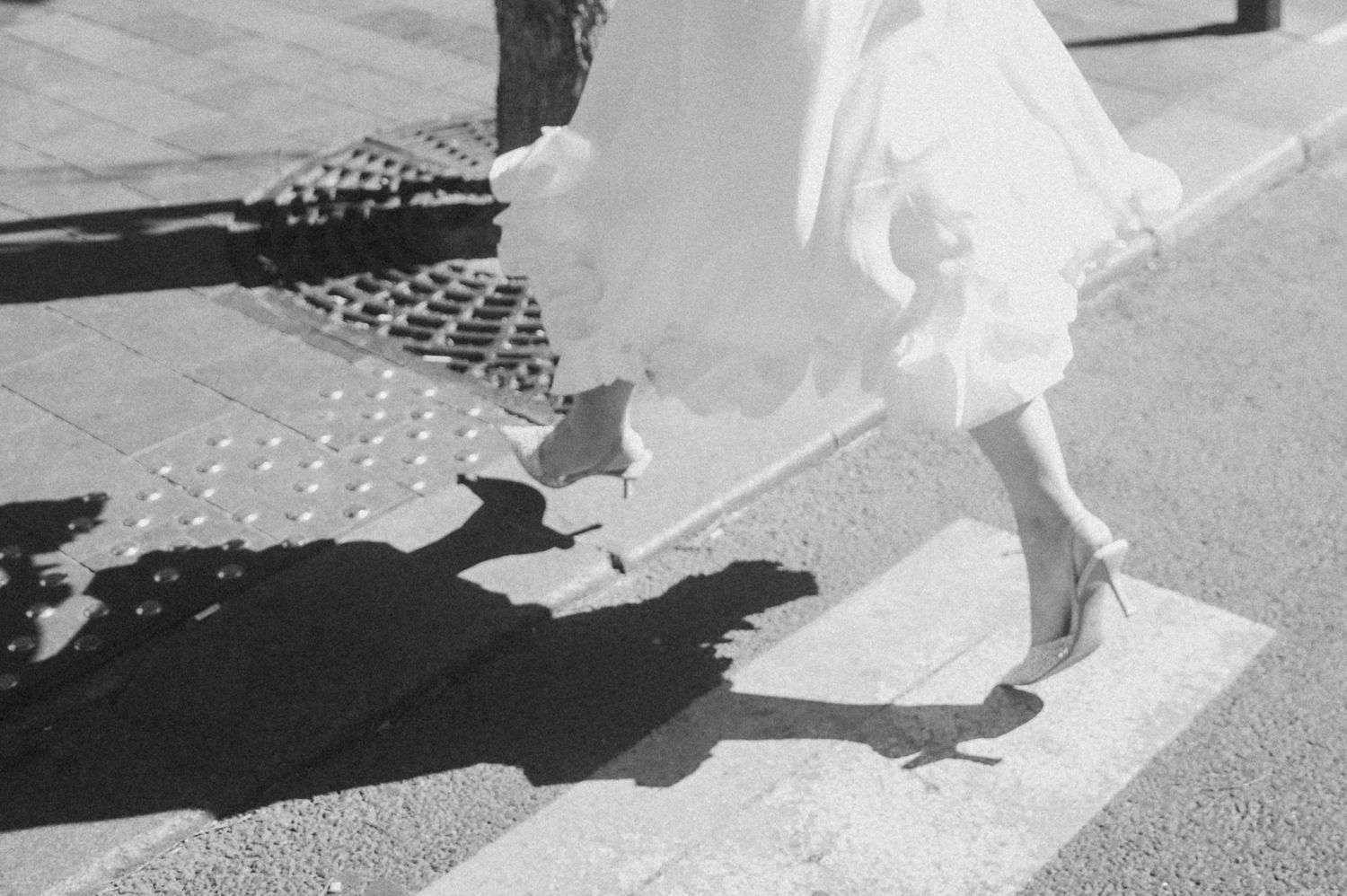A flowing white dress and shoes cast dramatic shadows on a sunlit pavement.