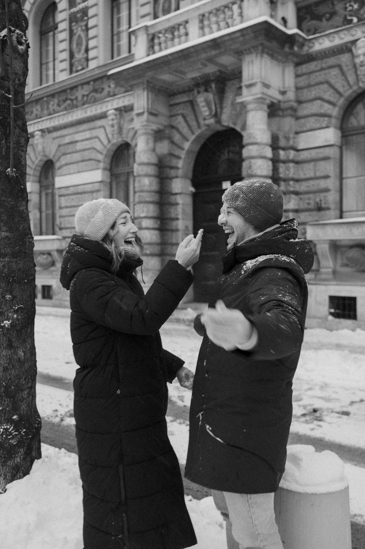 Two people in winter coats sharing a playful moment in front of a historic building.
