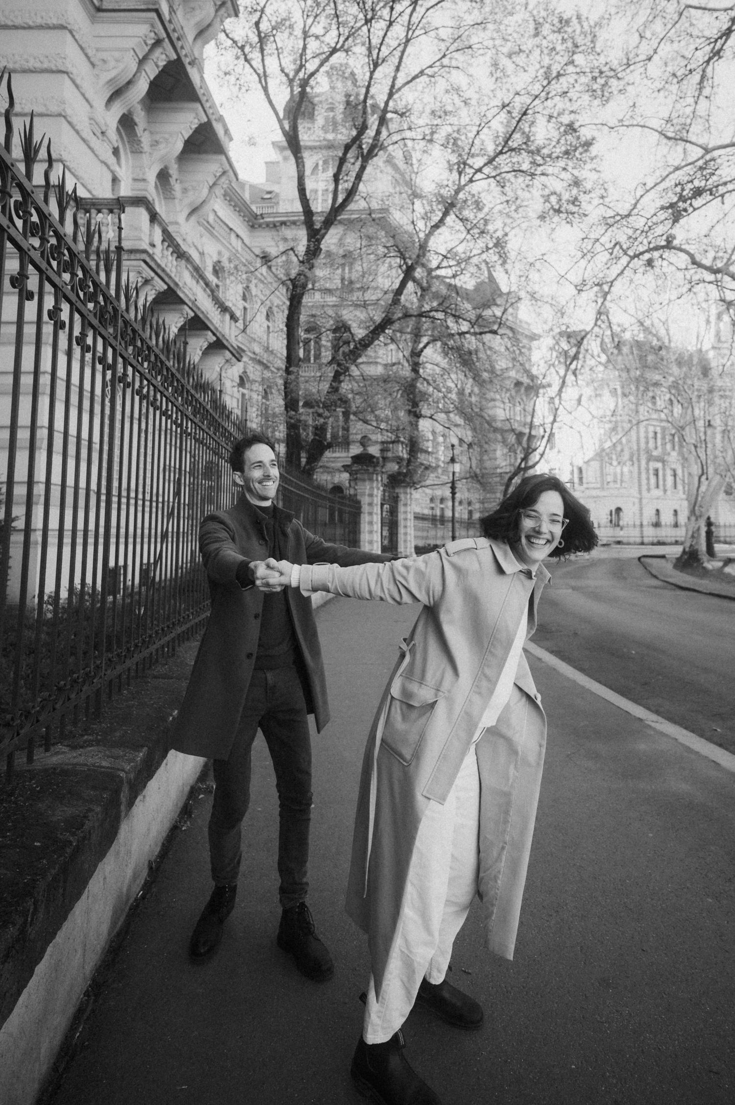 Black and white photo sequence showing two people walking and interacting along a path with iron fence and trees.