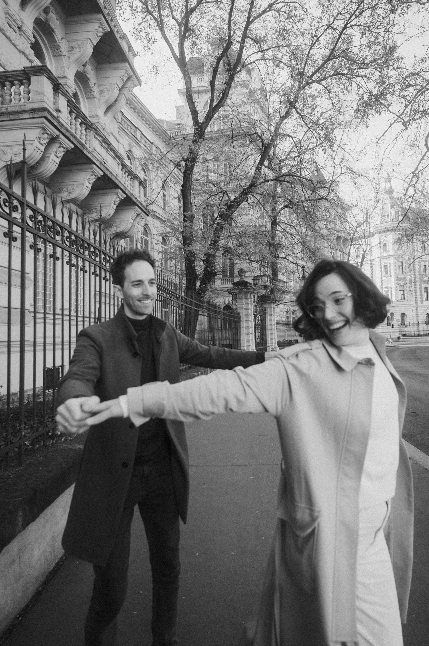 Black and white photo series showing two people dancing and moving playfully along an iron fence on a city street.