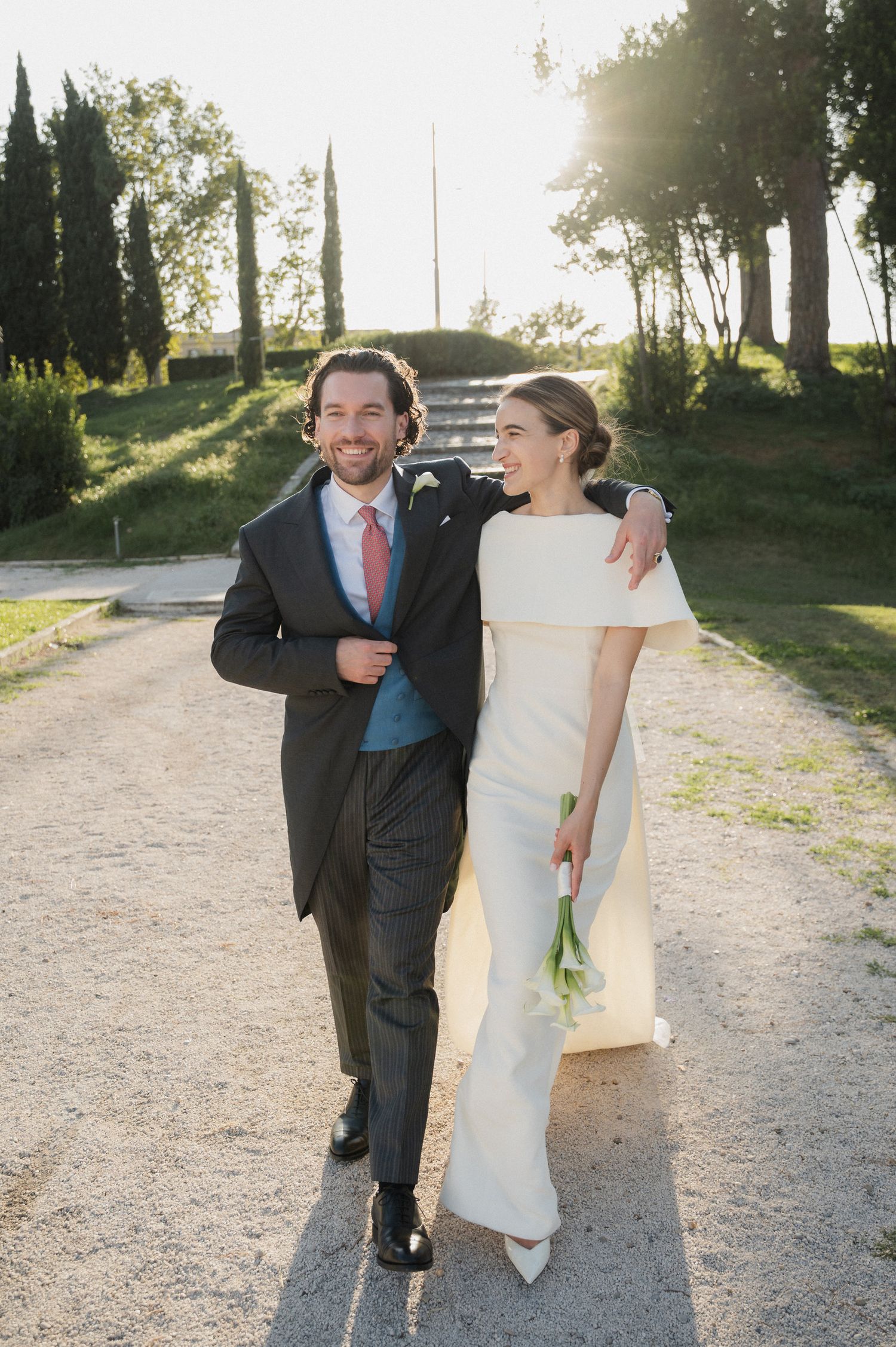 Newlyweds laugh together while walking down a scenic outdoor path during golden hour.