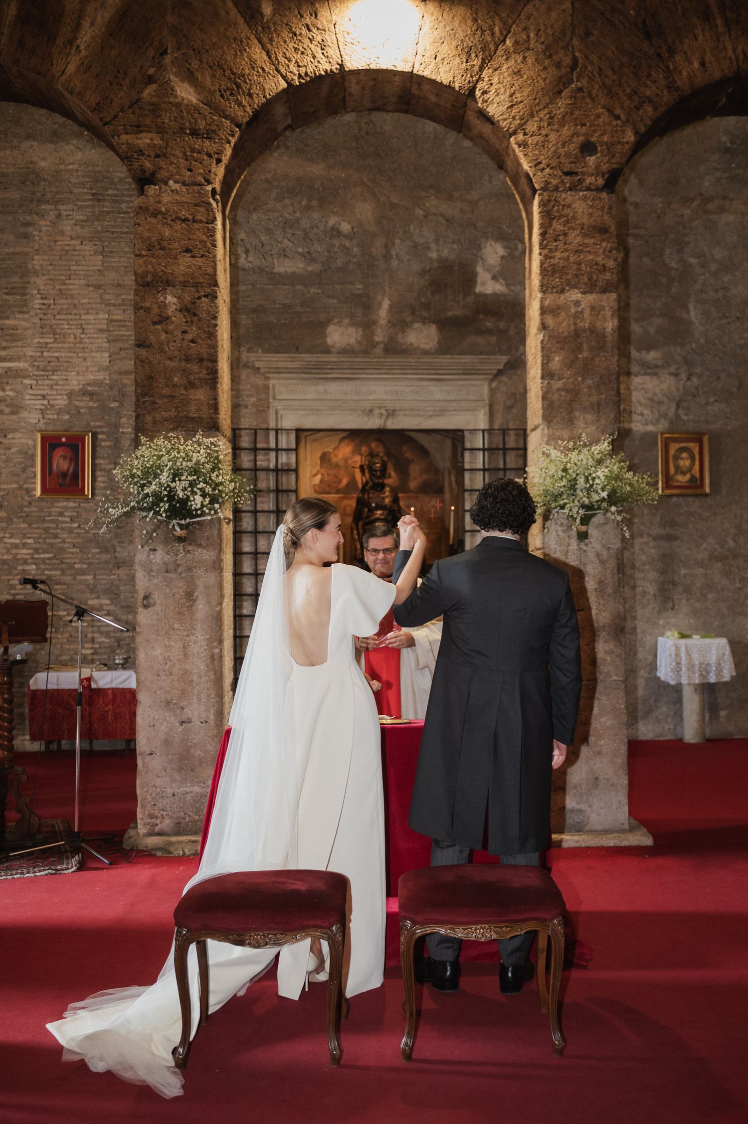 Wedding ceremony in historic brick archway venue with red carpet and religious decor.