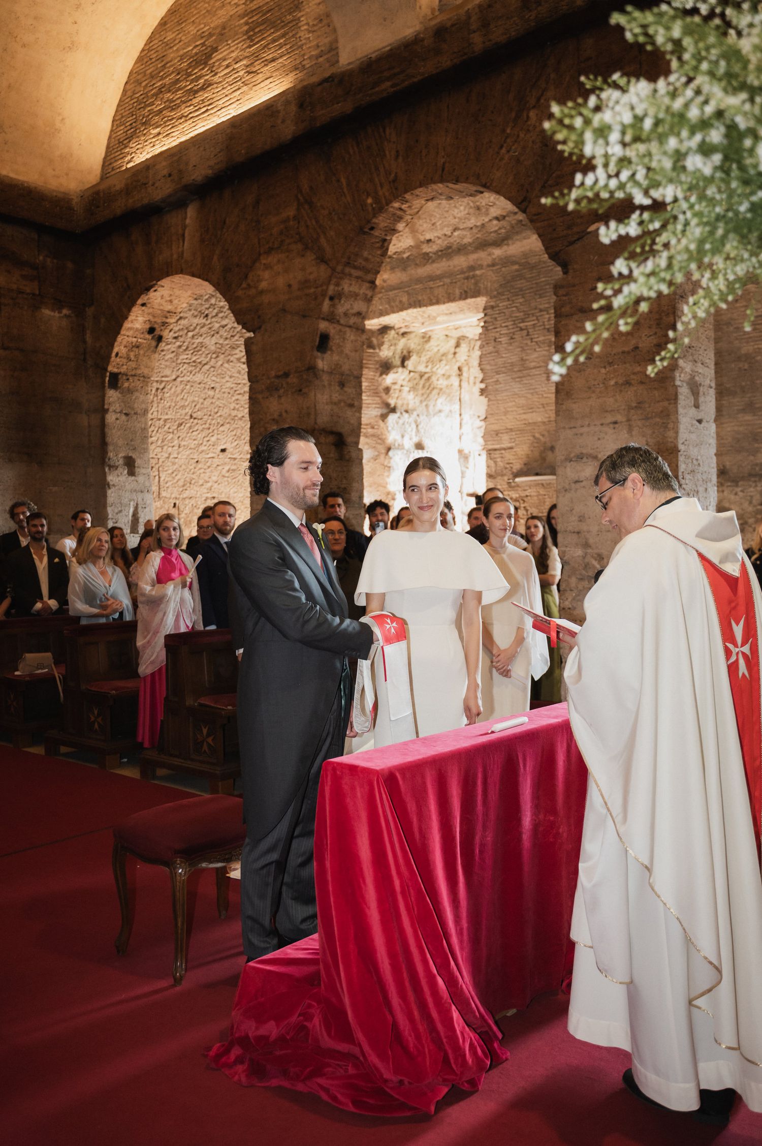 Wedding ceremony in a rustic stone chapel with vaulted ceilings and red ceremonial decorations.