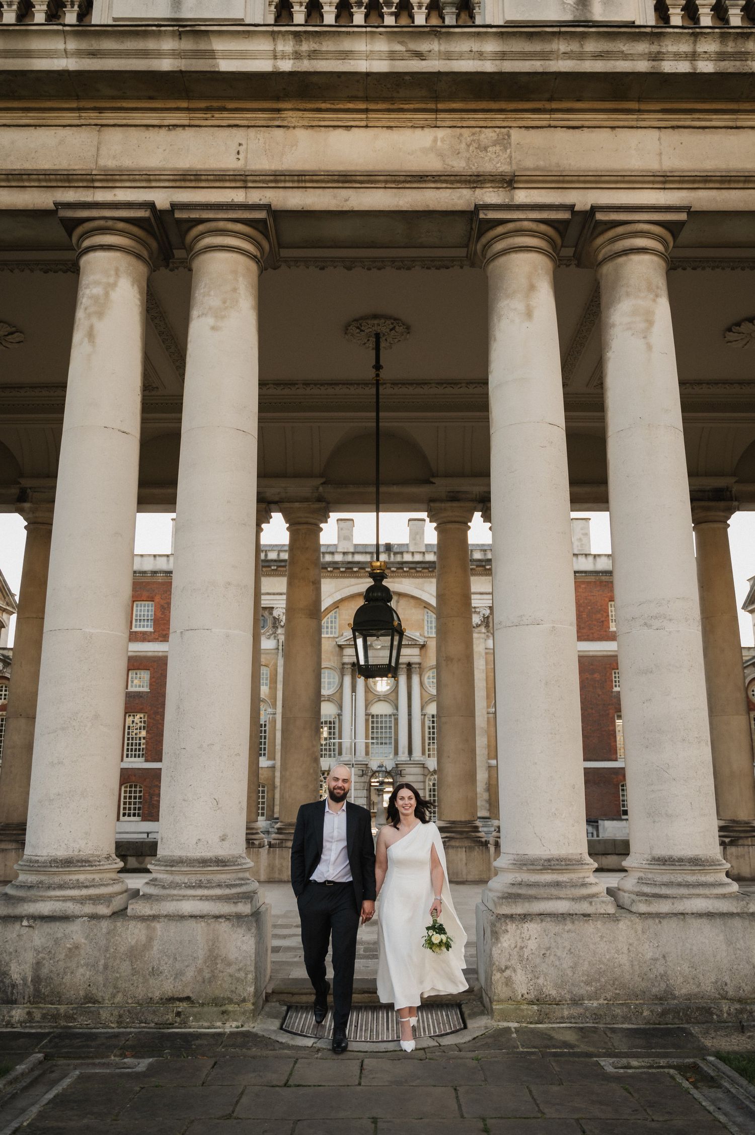 A couple stands beneath grand classical columns with ornate architectural details.