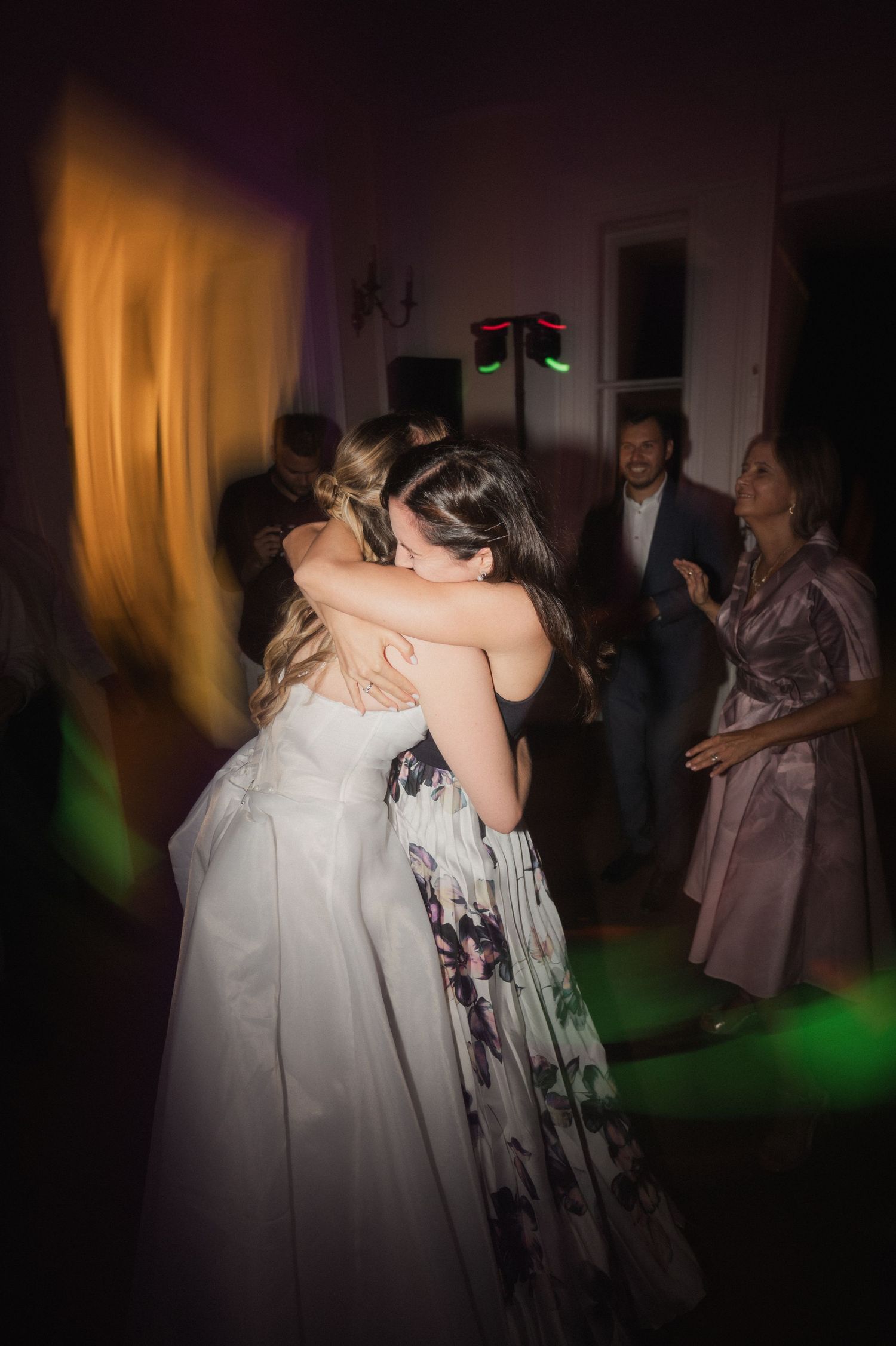 Bride sharing heartfelt hug with guest on colorful dance floor at lively wedding reception.