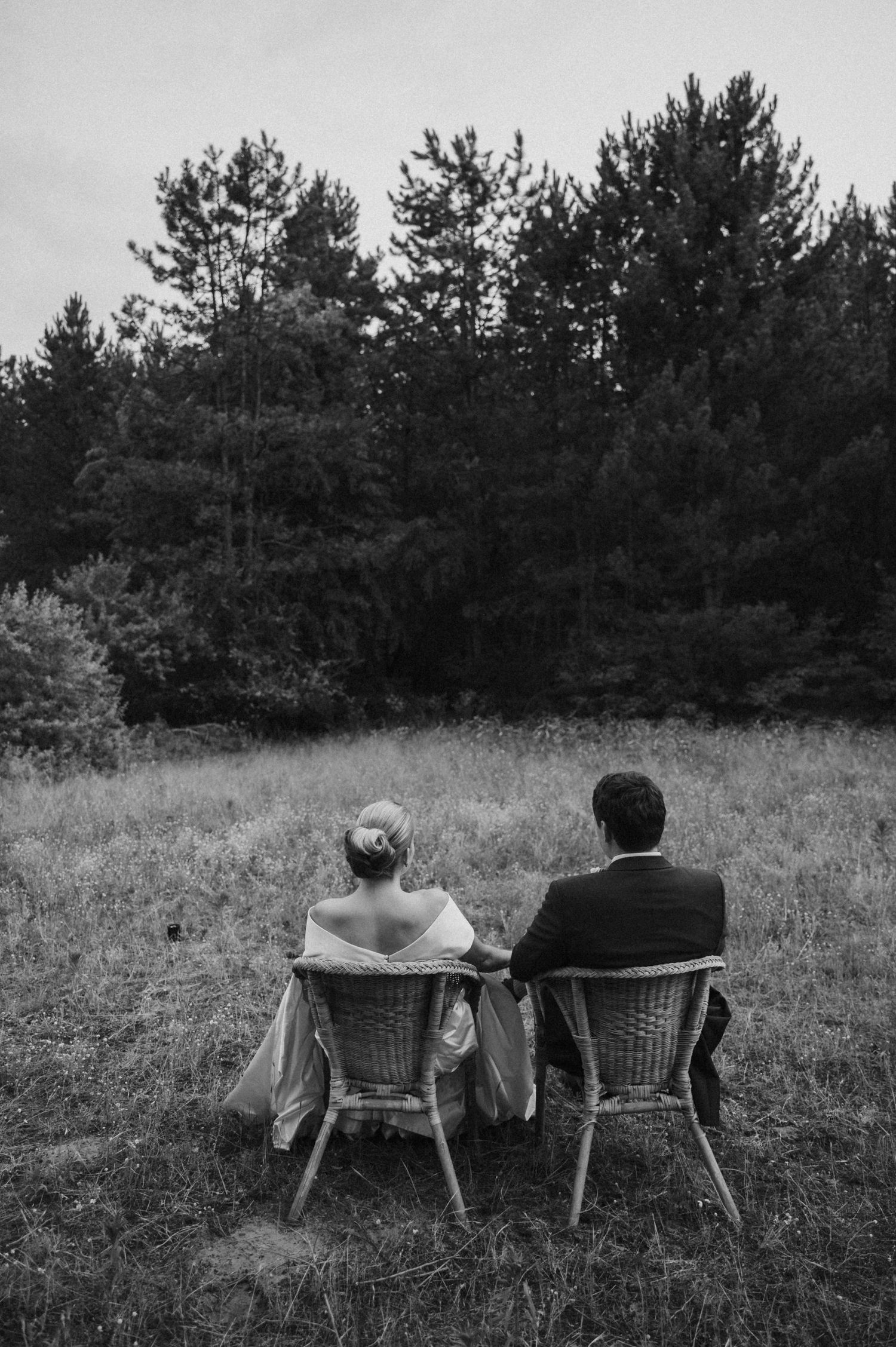 Couple relaxing in chairs against a backdrop of evergreen trees.