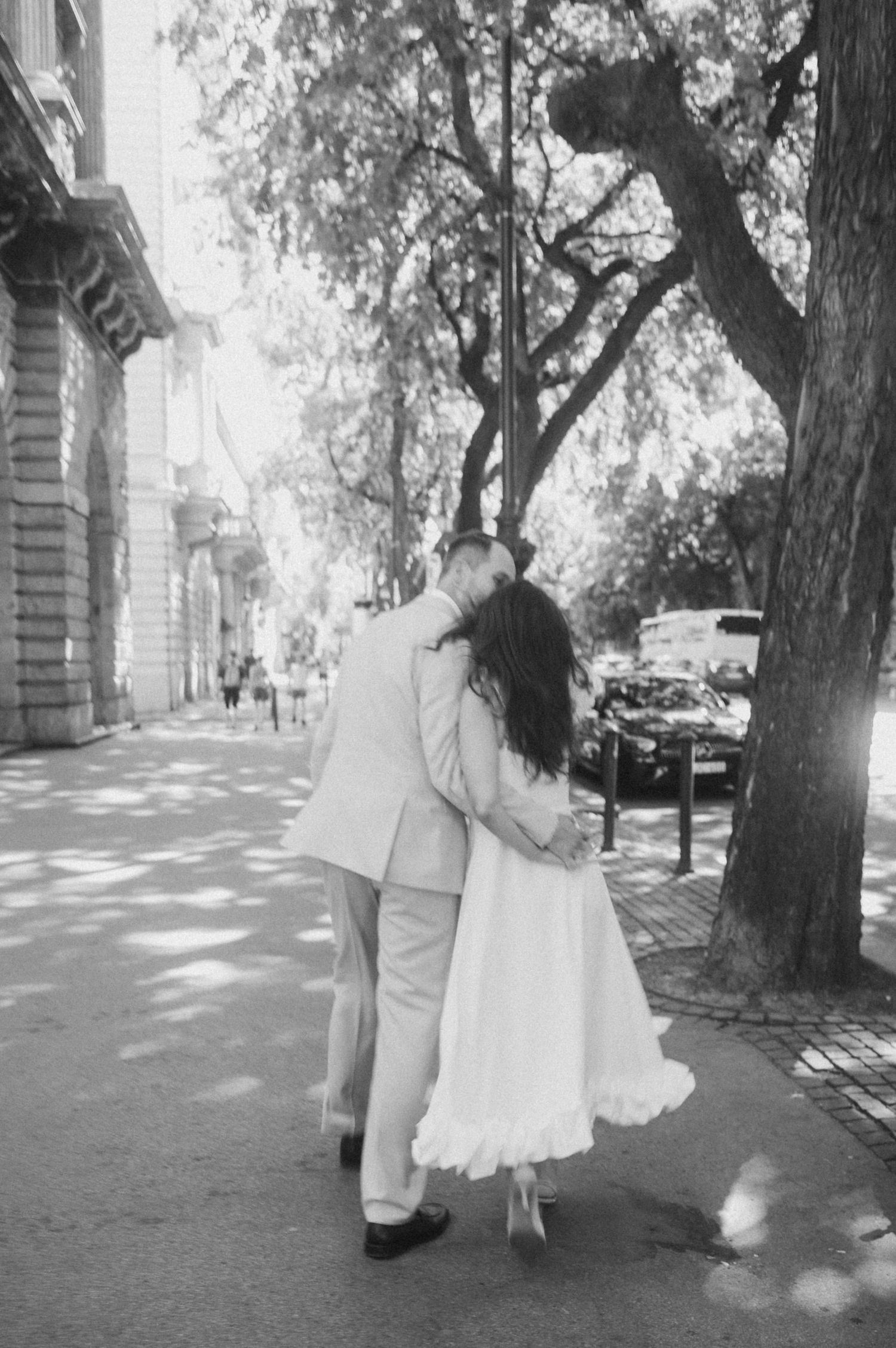 A romantic black and white photo of a couple embracing on a tree-lined street.