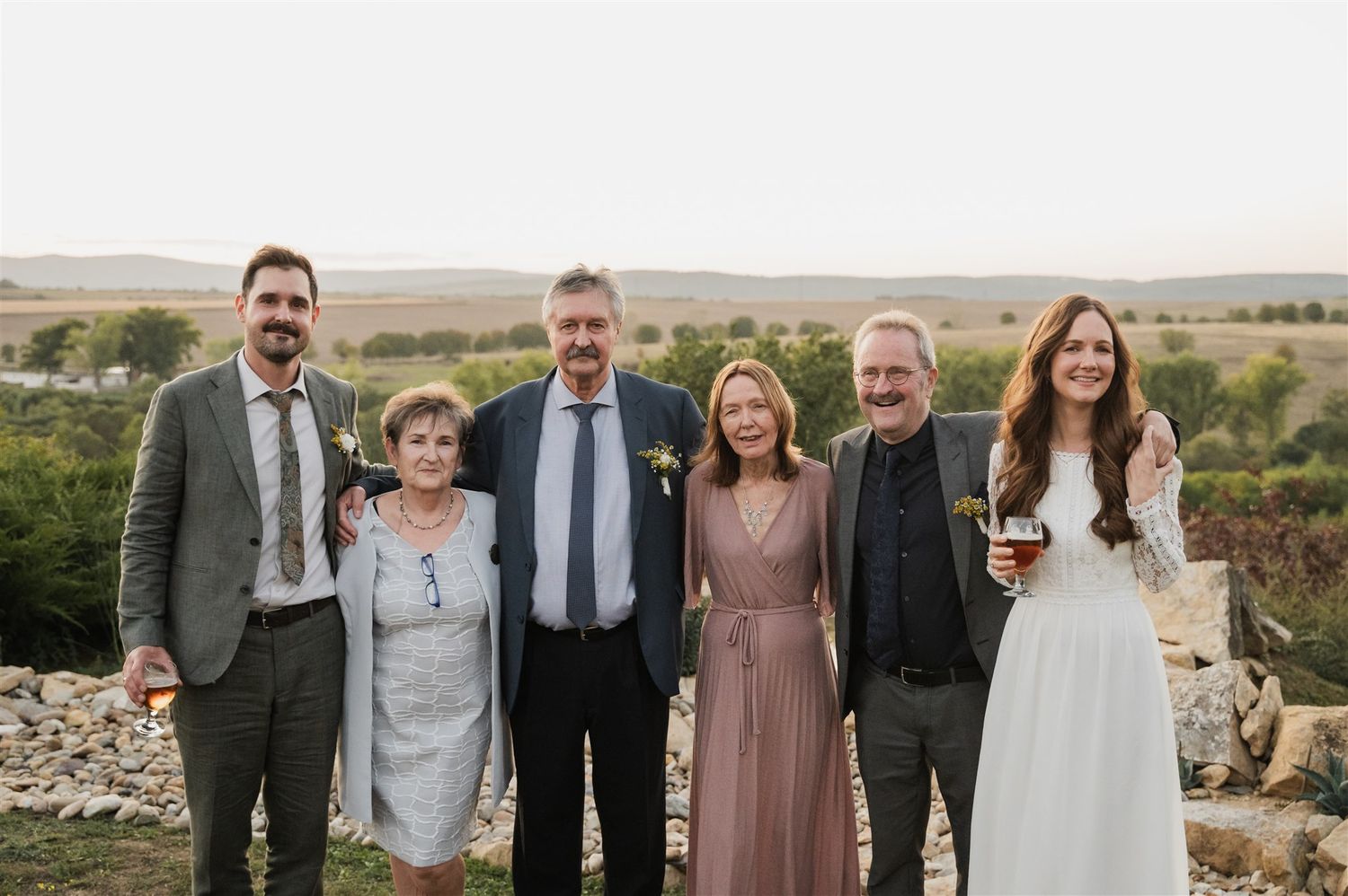 Wedding party poses for group photos at sunset with mountains in the background.