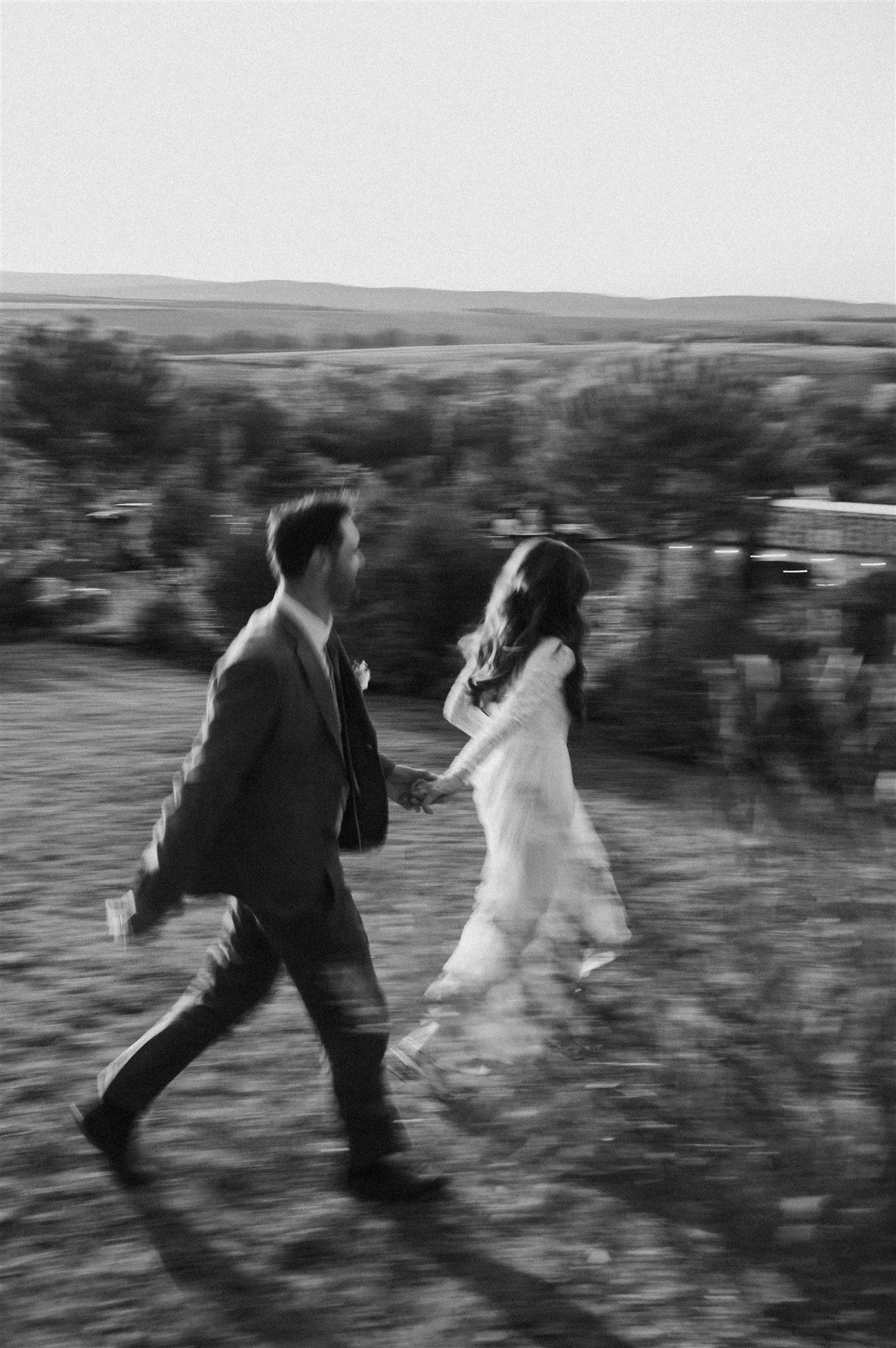 Motion-blurred black and white photo of two people running across a hillside landscape.