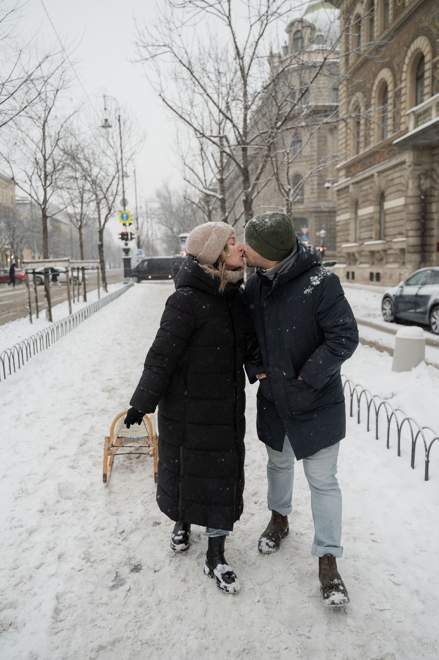 A couple sharing an intimate moment while holding a vintage sled in the snow.