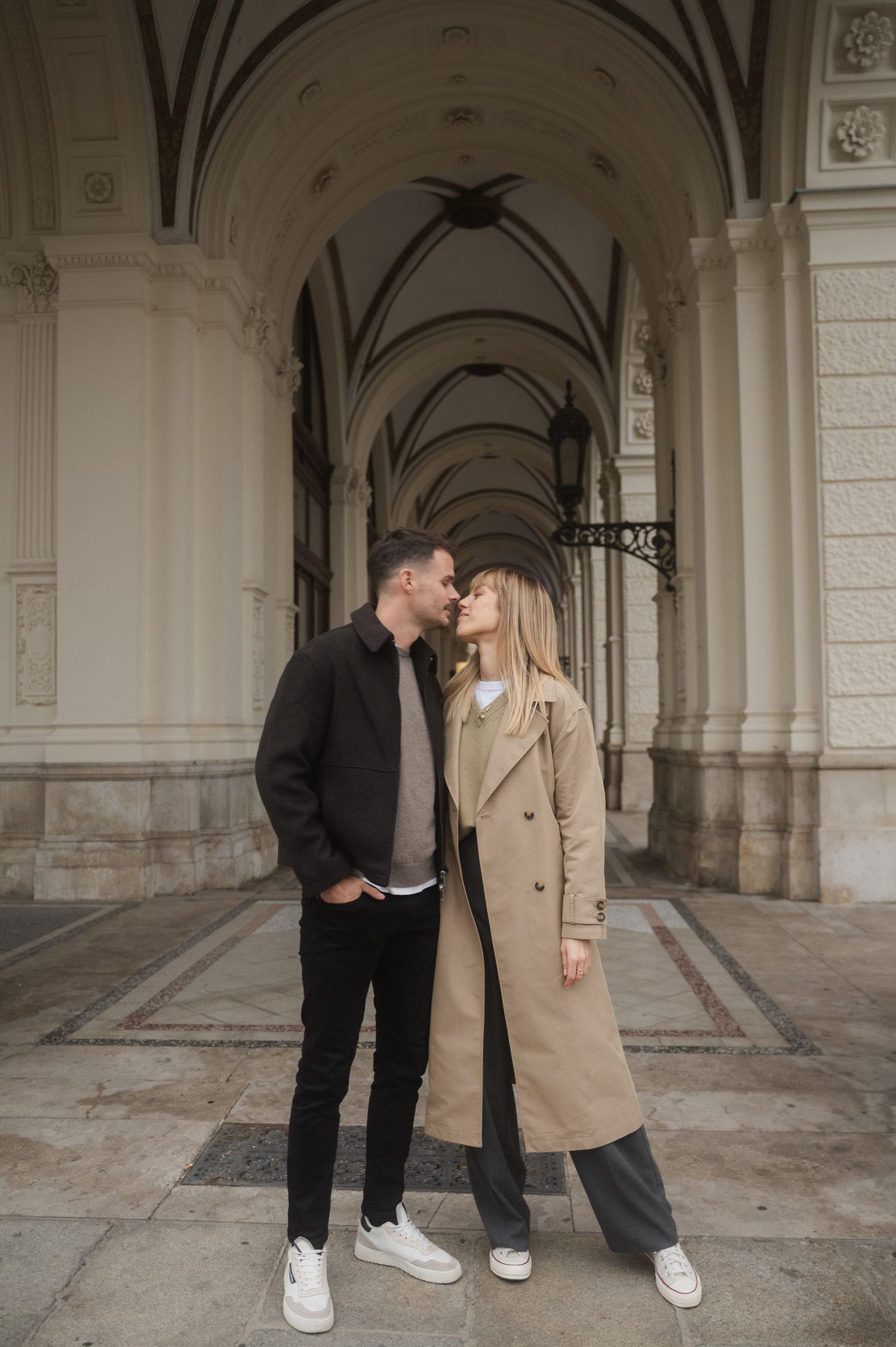 A couple in casual attire sharing an intimate moment under ornate arched hallway with vaulted ceilings.