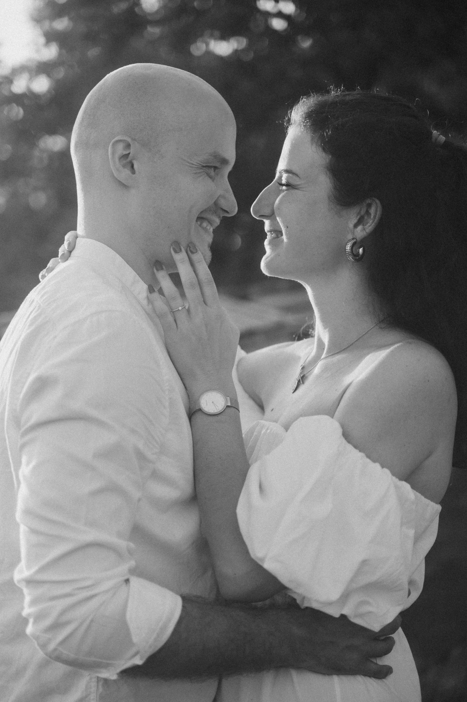 A black and white portrait captures an intimate moment between a couple in matching white attire.