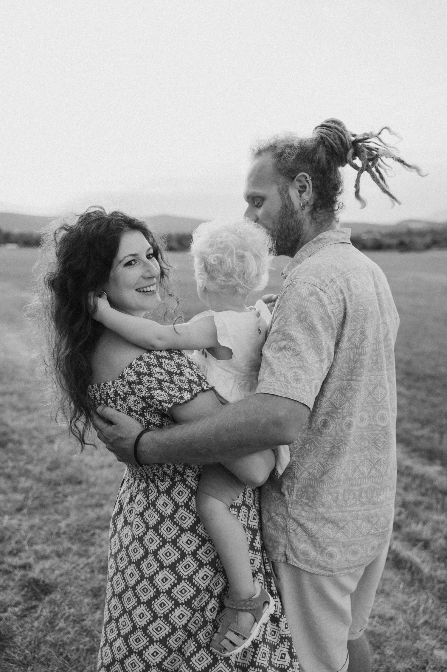 A couple embraces and dances together in a grassy field at sunset in a series of romantic black and white photos.