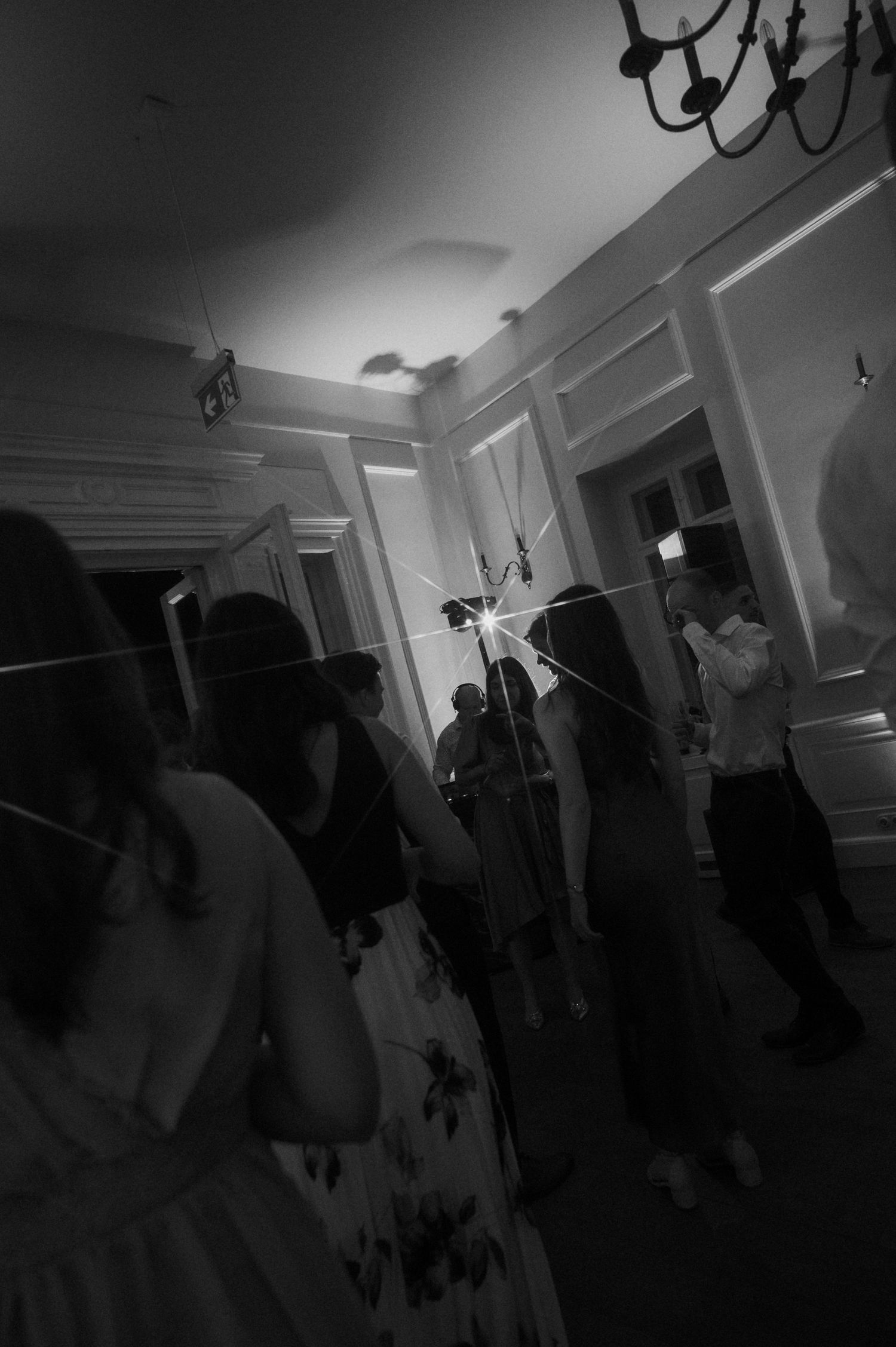 Black and white photo of wedding guests dancing with sparklers creating light streaks in elegant reception venue.