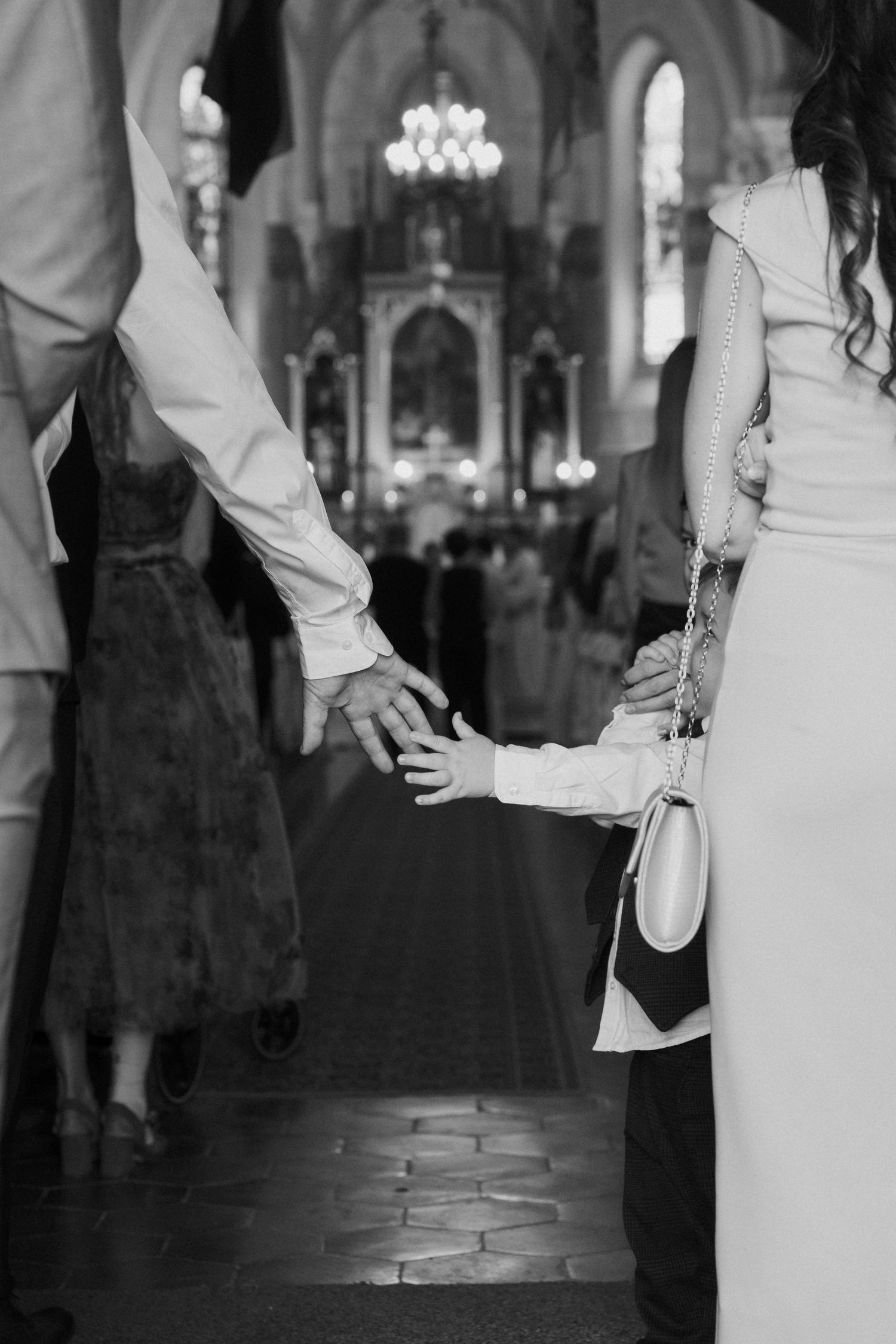 Black and white photo of bride and groom holding hands with child during church wedding ceremony.