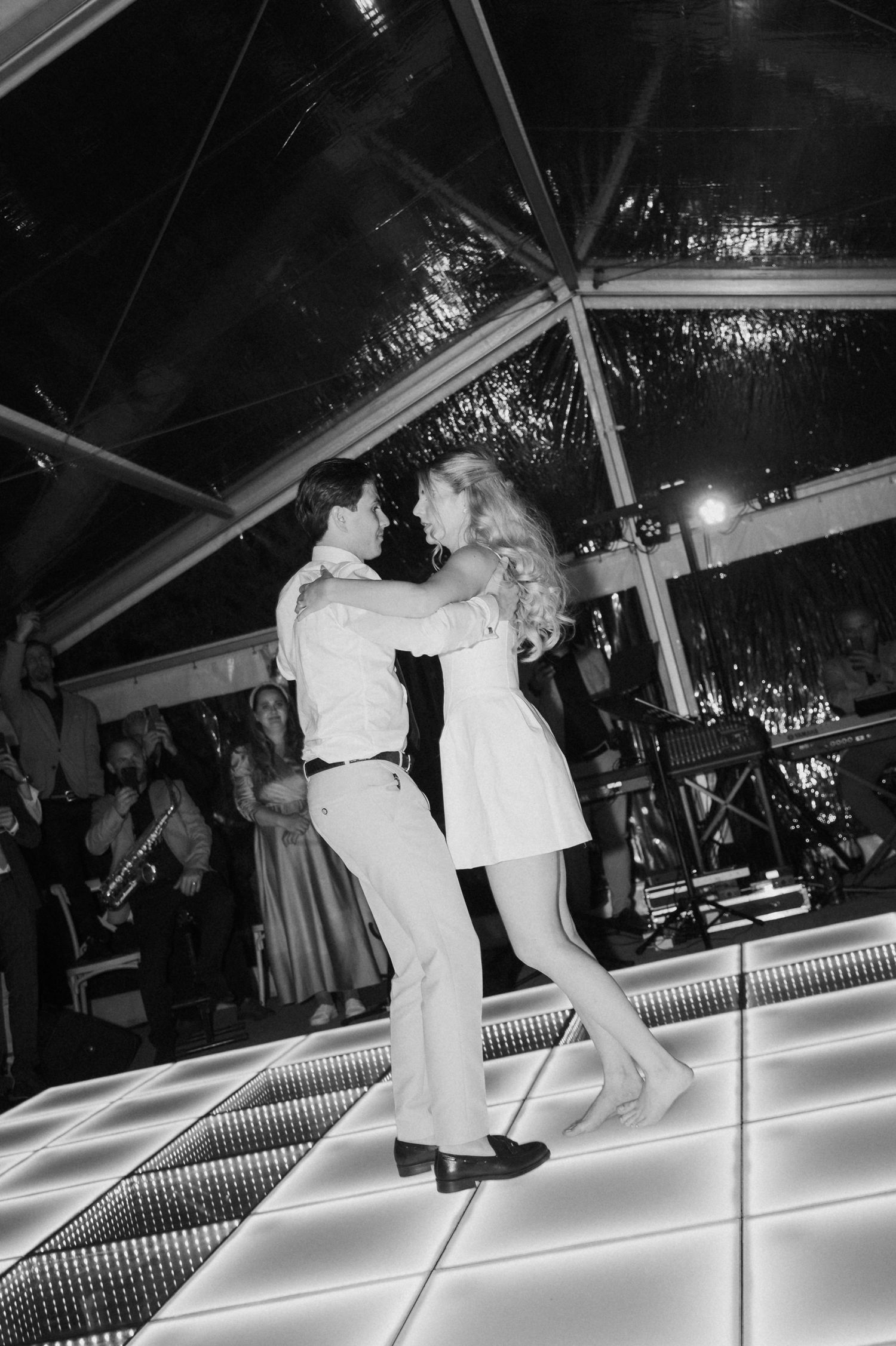 Bride and groom sharing their first dance on a lit dance floor in black and white wedding photo.