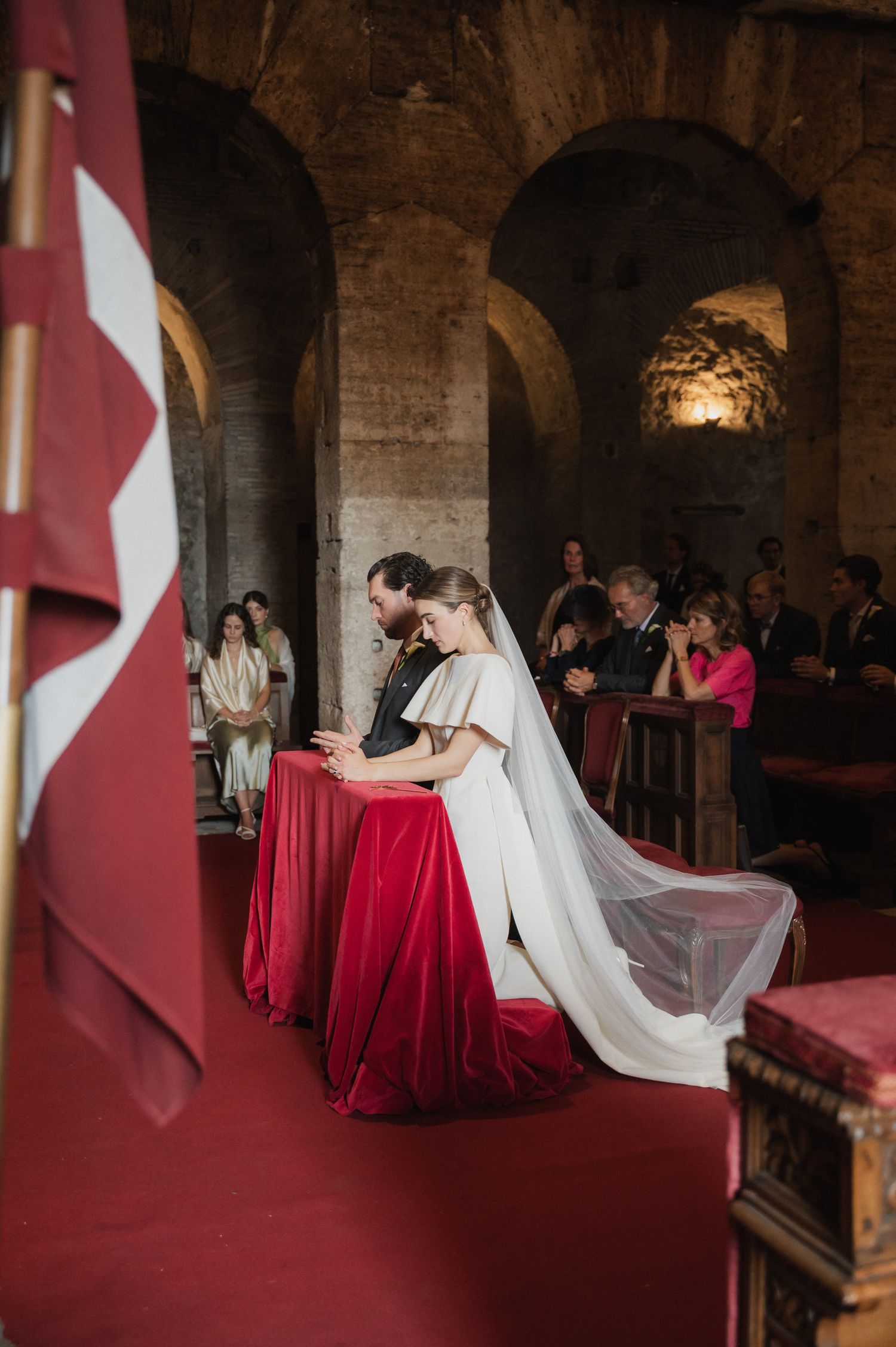 Wedding ceremony in rustic stone venue with red carpet and dramatic lighting.