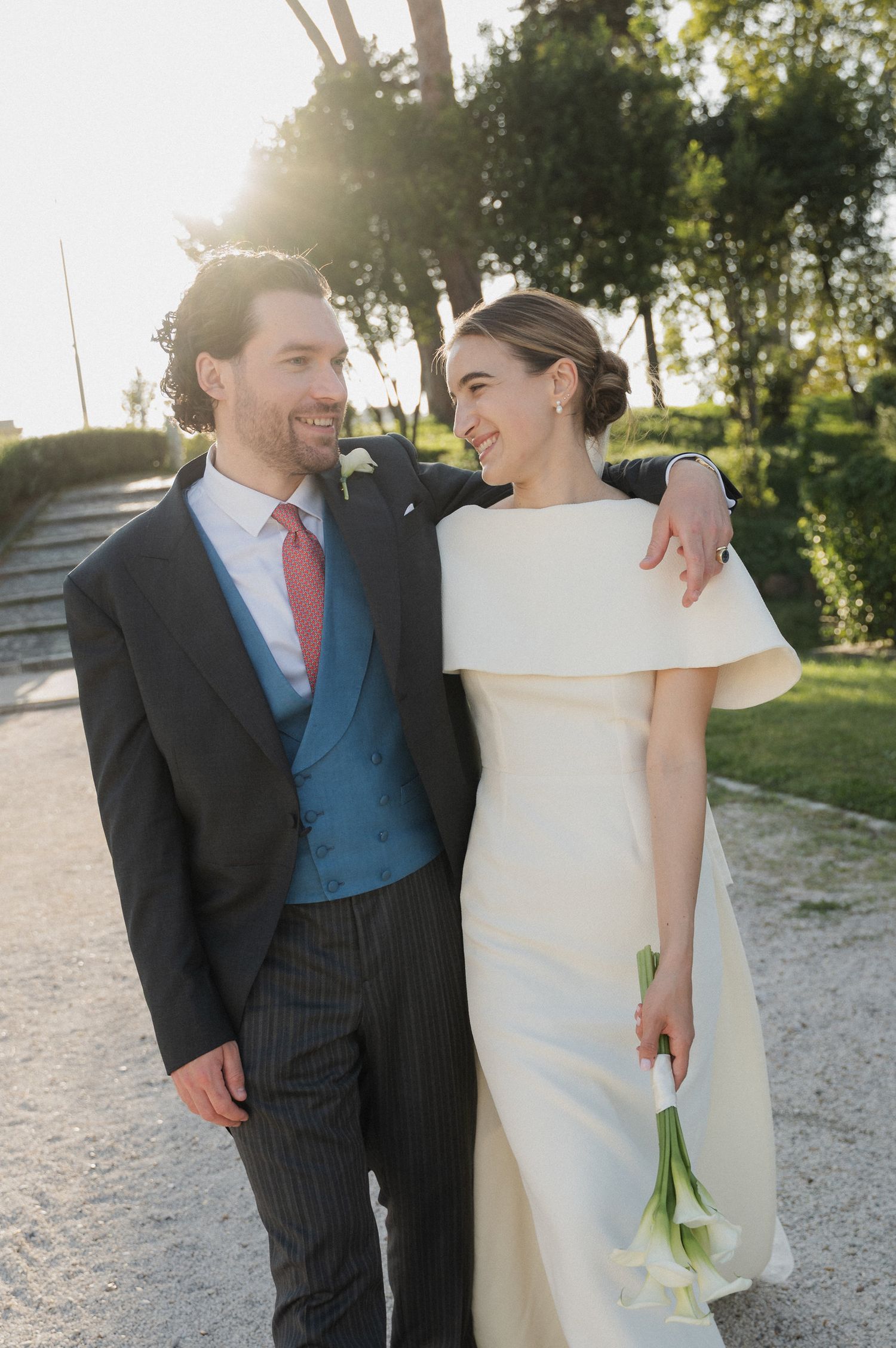 Wedding couple in formal attire shares intimate moments on a sunny outdoor path.
