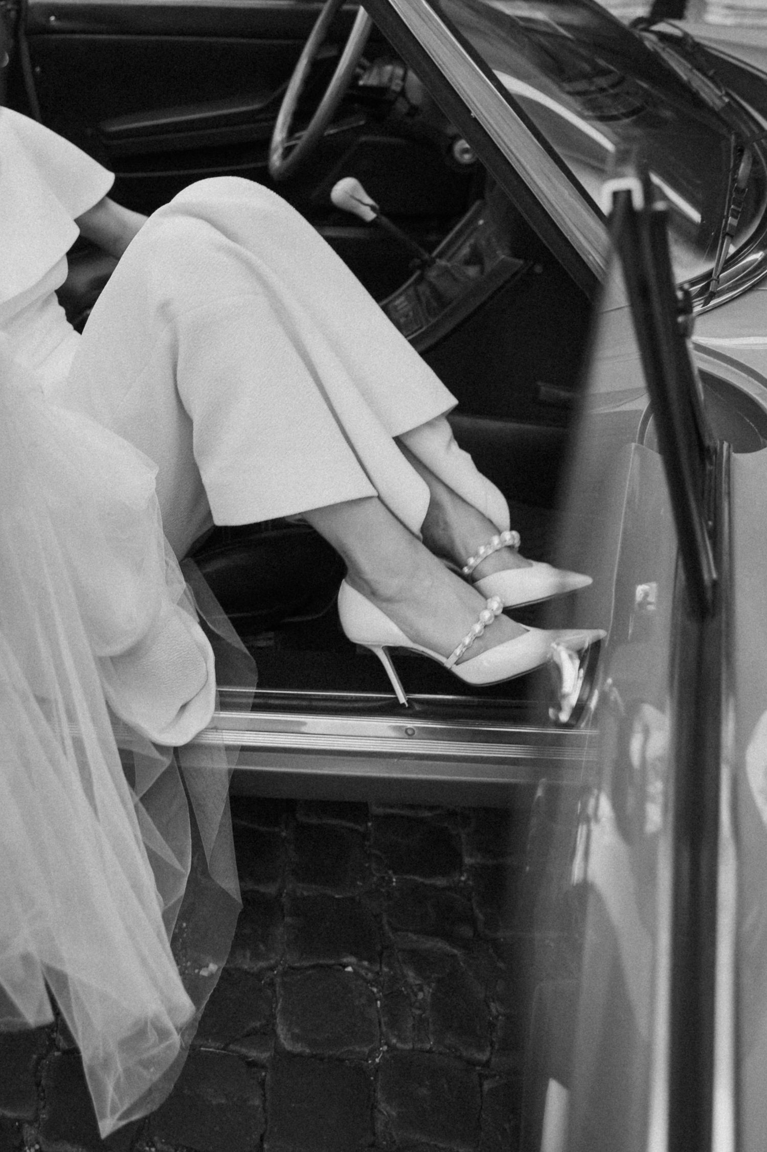 Sequence showing bride in white dress getting into vintage red automobile.