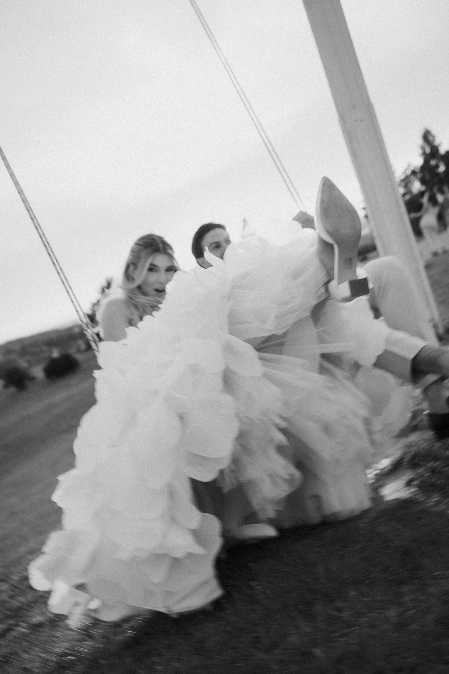 Black and white candid photo of bride and groom playfully swinging together on their wedding day.