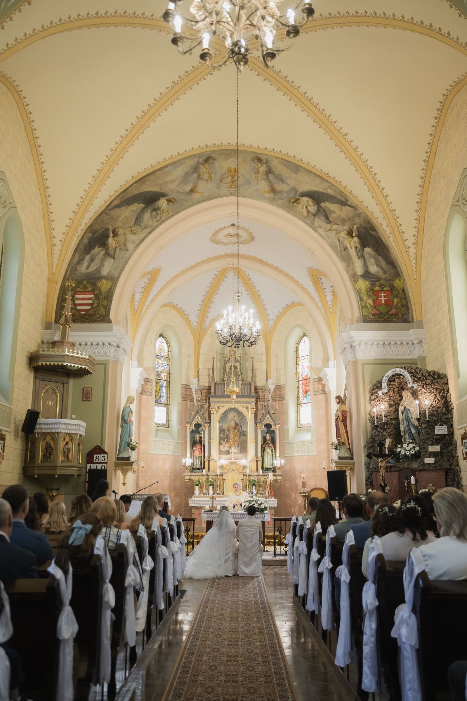 Wide-angle view of a church wedding ceremony with guests seated in white pews and ornate altar.
