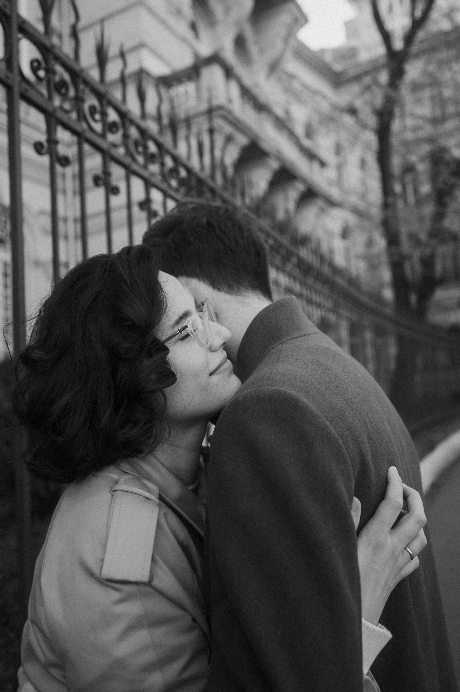 A romantic black and white photograph of a couple embracing near an ornate iron gate.