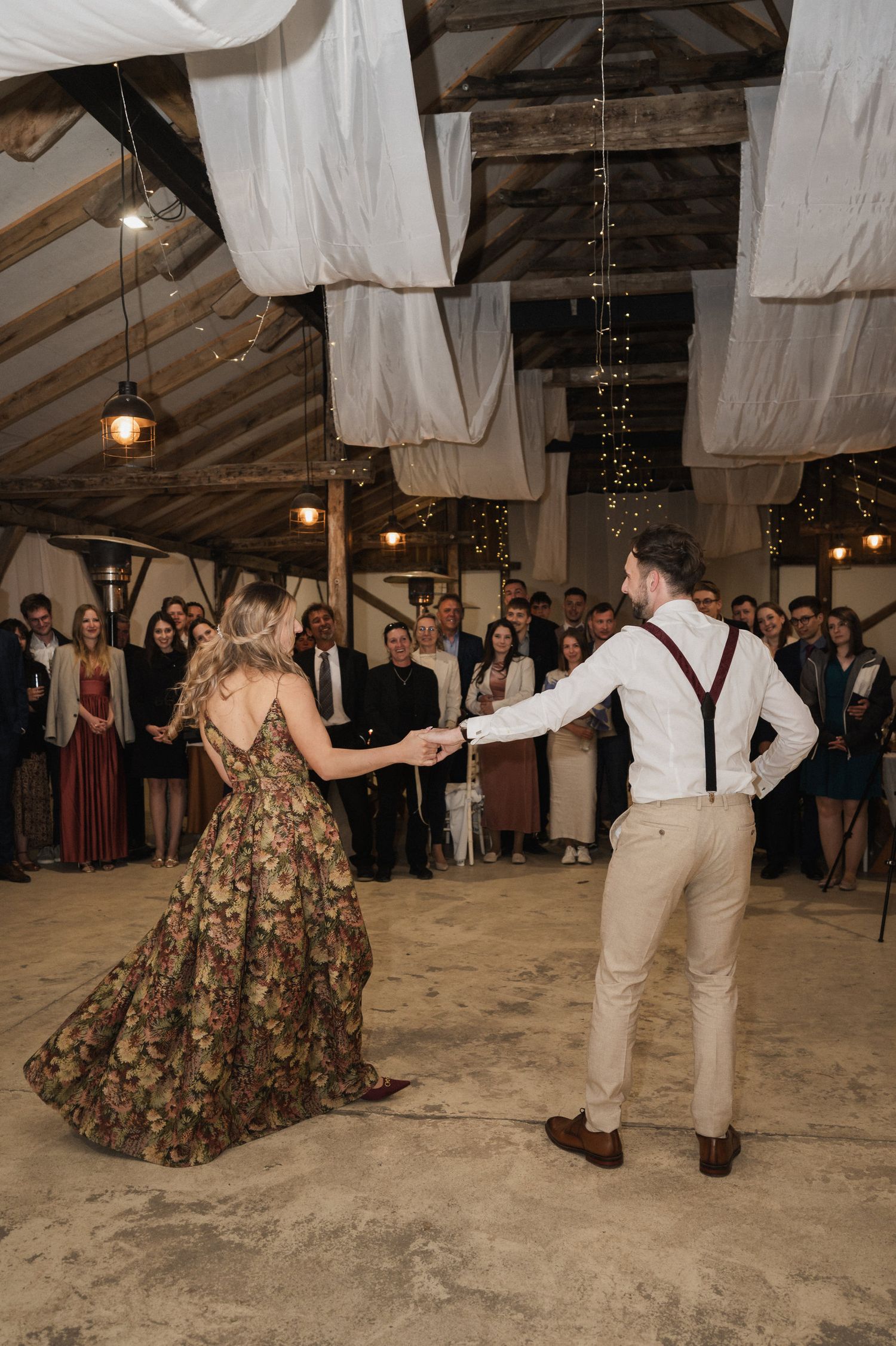 Couples dancing at a rustic wedding reception with white fabric draped from ceiling and sand covered floor.