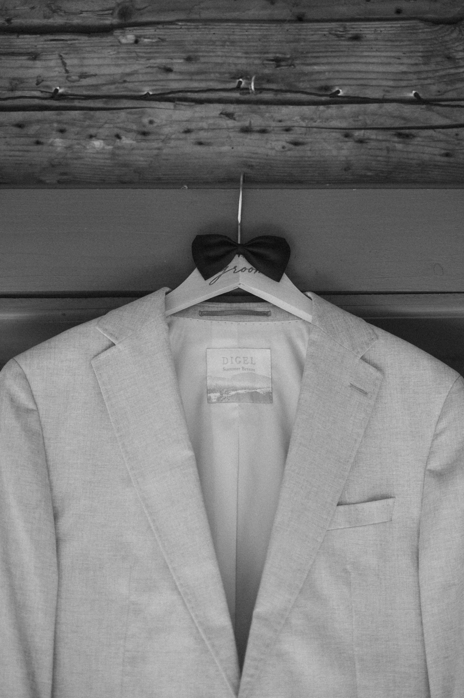 A row of identical light gray suit jackets hanging on wooden hangers against a rustic wooden wall background.