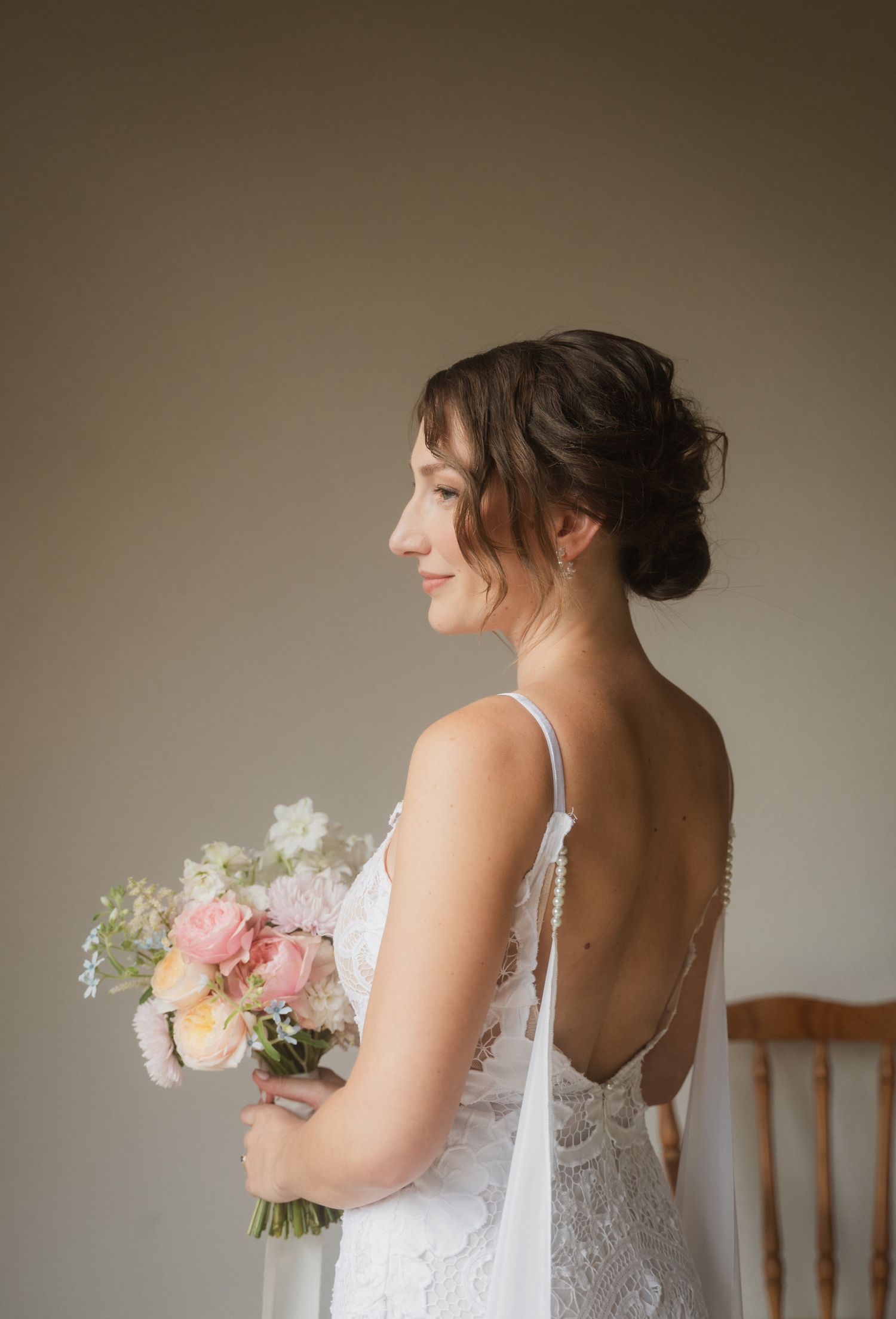 A bride in a lace gown holds a bouquet while showing the elegant open back of her dress.