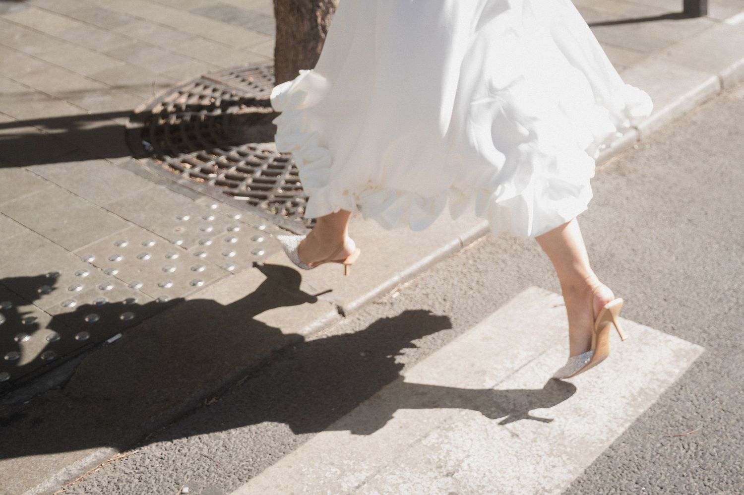 Wedding dress and shoes detail shot on sunny urban sidewalk.