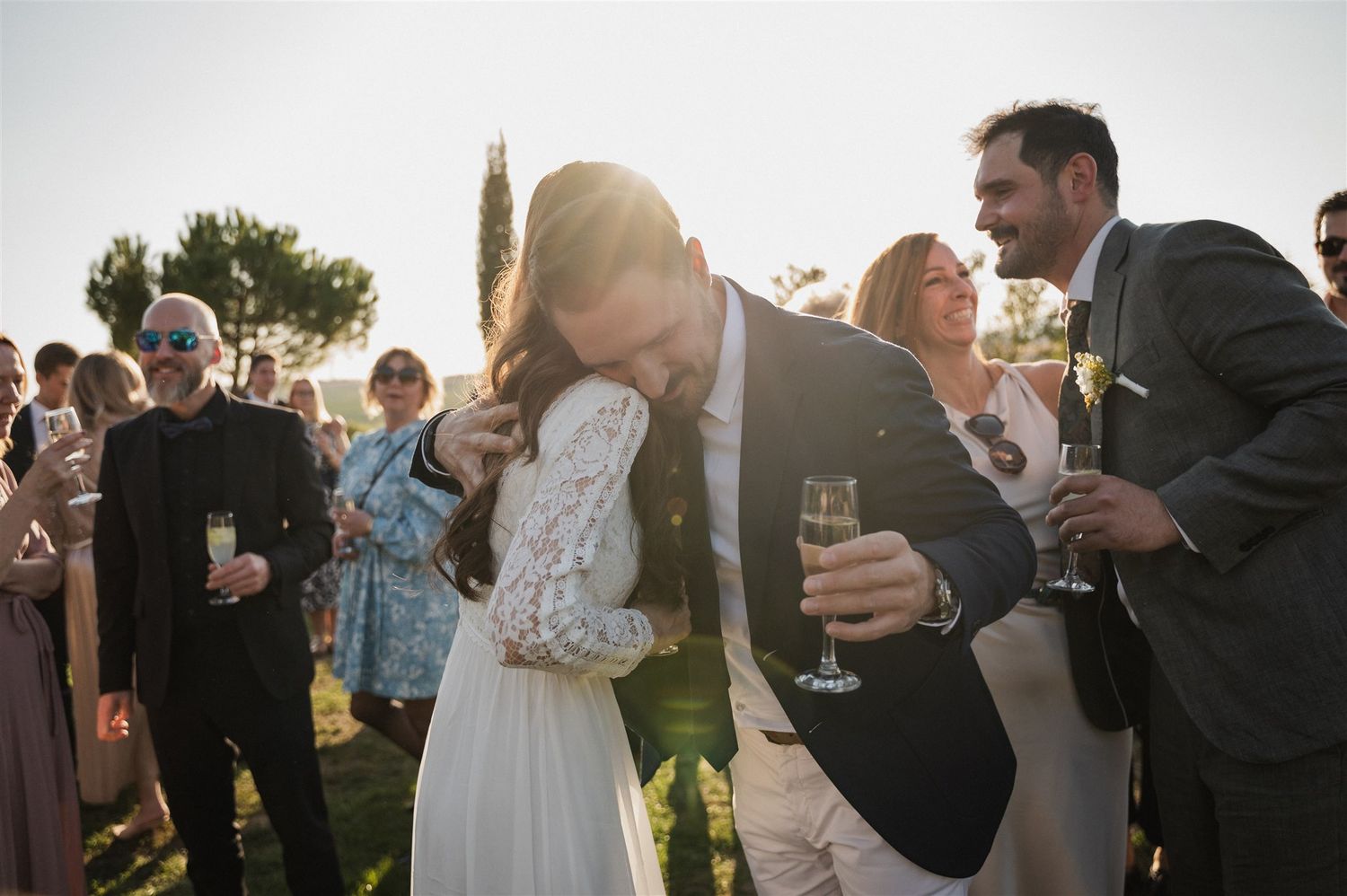 Wedding guests mingle and toast during an outdoor cocktail reception at sunset.