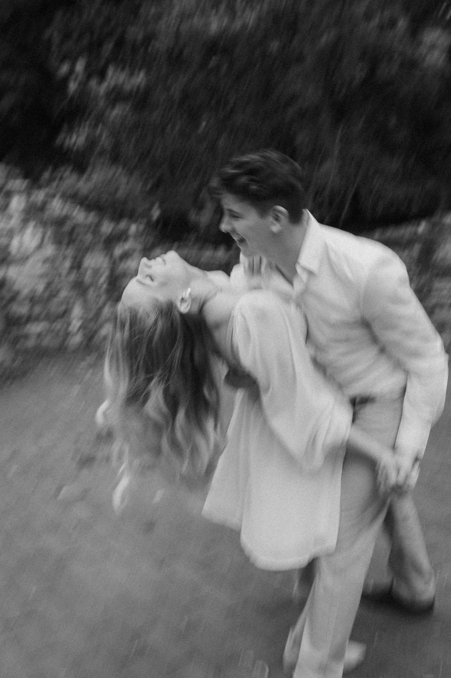 Motion-blurred black and white photo of a couple dancing together outdoors.