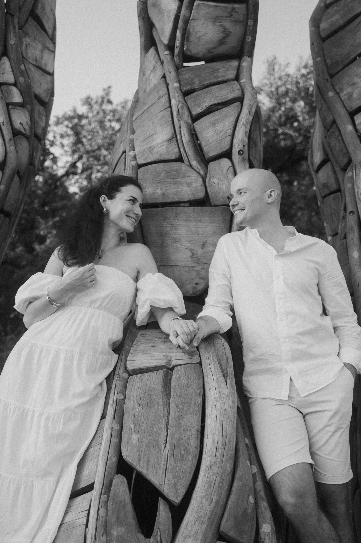 Black and white romantic photo series showing a couple in white outfits sharing intimate moments against a rustic wooden wall.